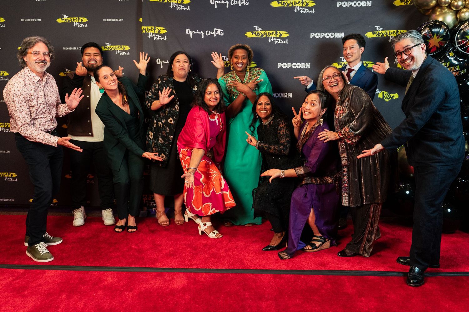 Diverse group of smiling people pose together on a red carpet at a film festival event.