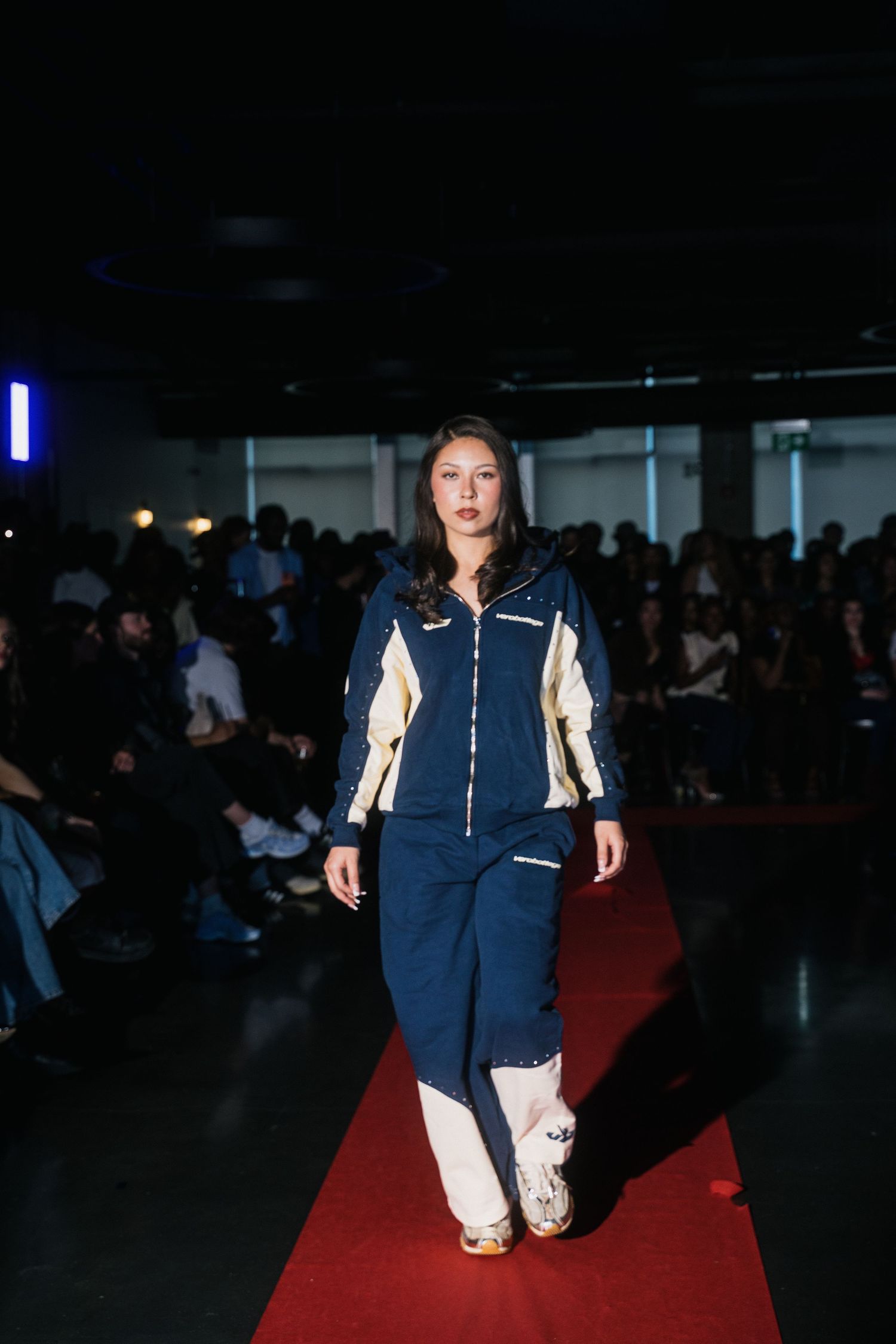 Female model walks red carpet runway in navy and cream tracksuit at a fashion show.