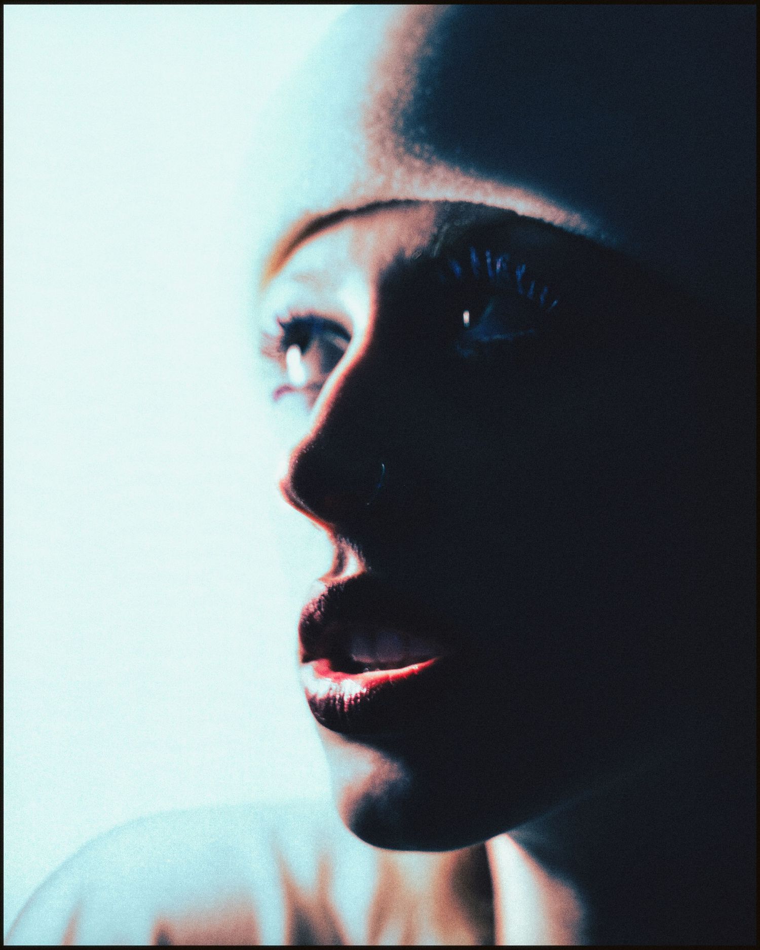 Dramatic close-up portrait of a person with red lips illuminated by blue light against dark background.