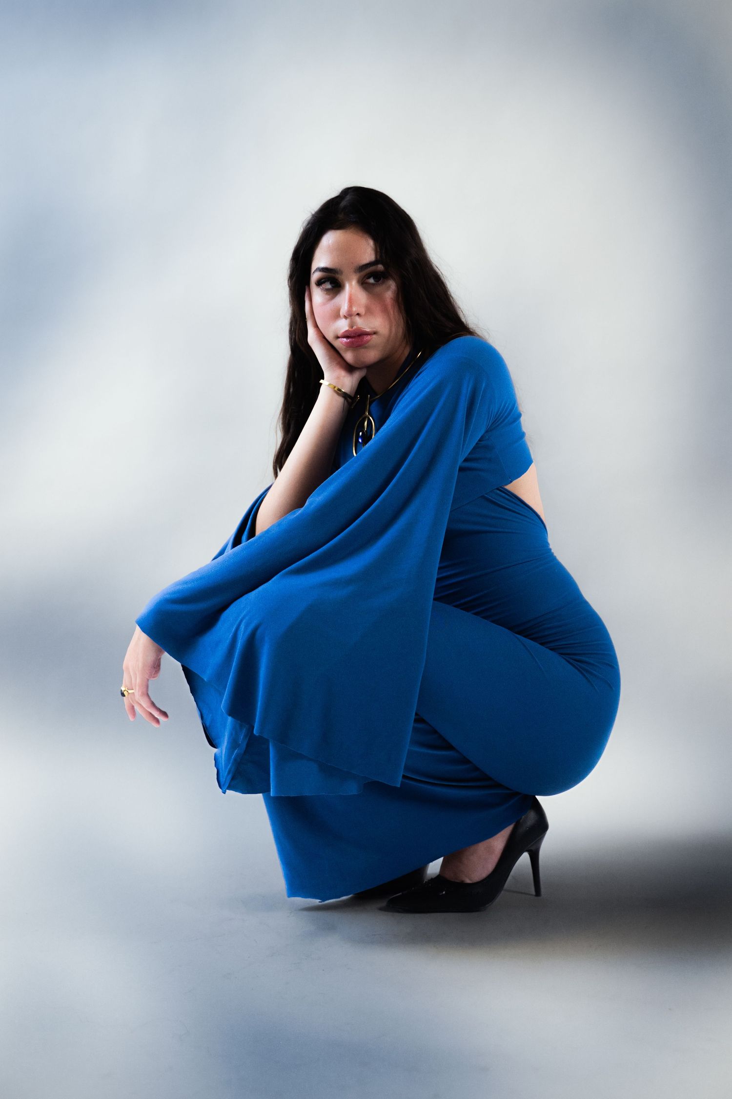 Woman in blue jumpsuit crouching on floor in studio.