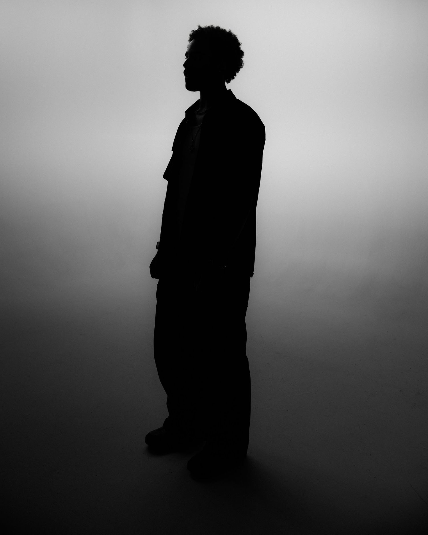 Black and white silhouette of a man standing against a soft gradient grey background.