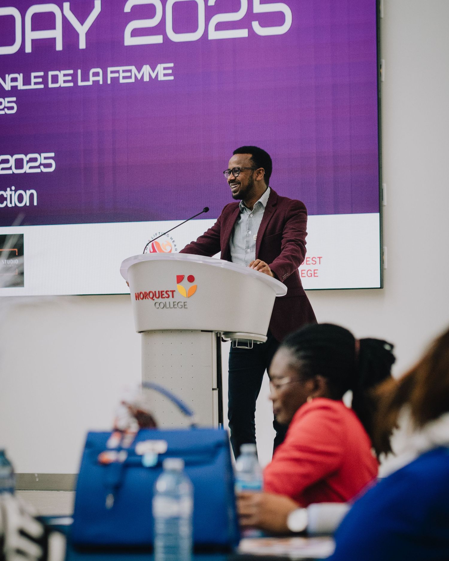 Speaker presents at podium during International Womens Day 2025 event at NorQuest College.