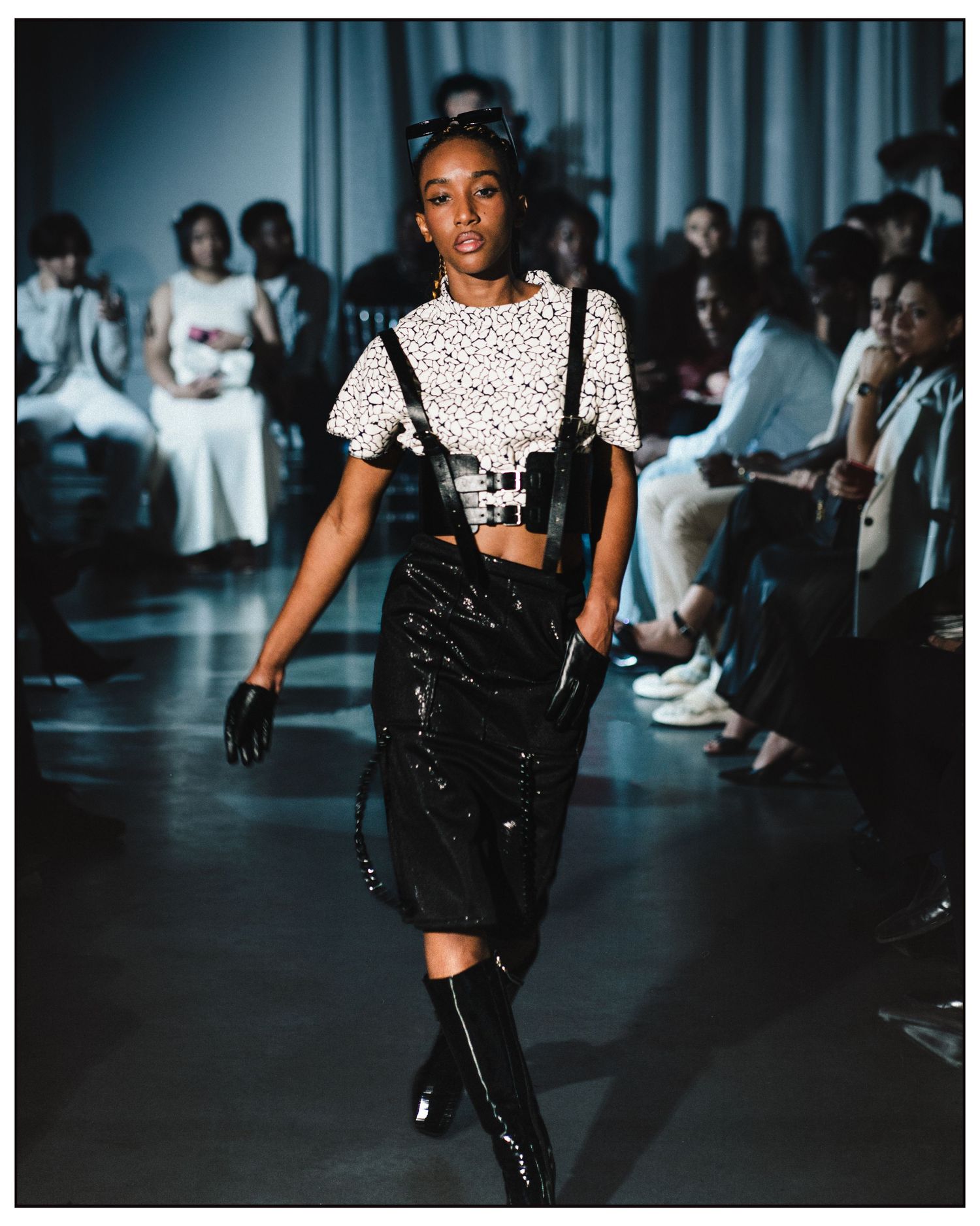 Model walks runway in polka dot crop top, black patent suspender skirt, and knee-high boots.