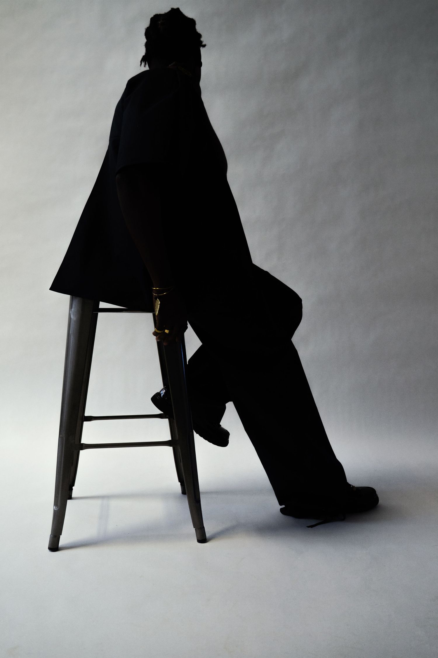 Silhouette of person sitting on stool in black outfit.