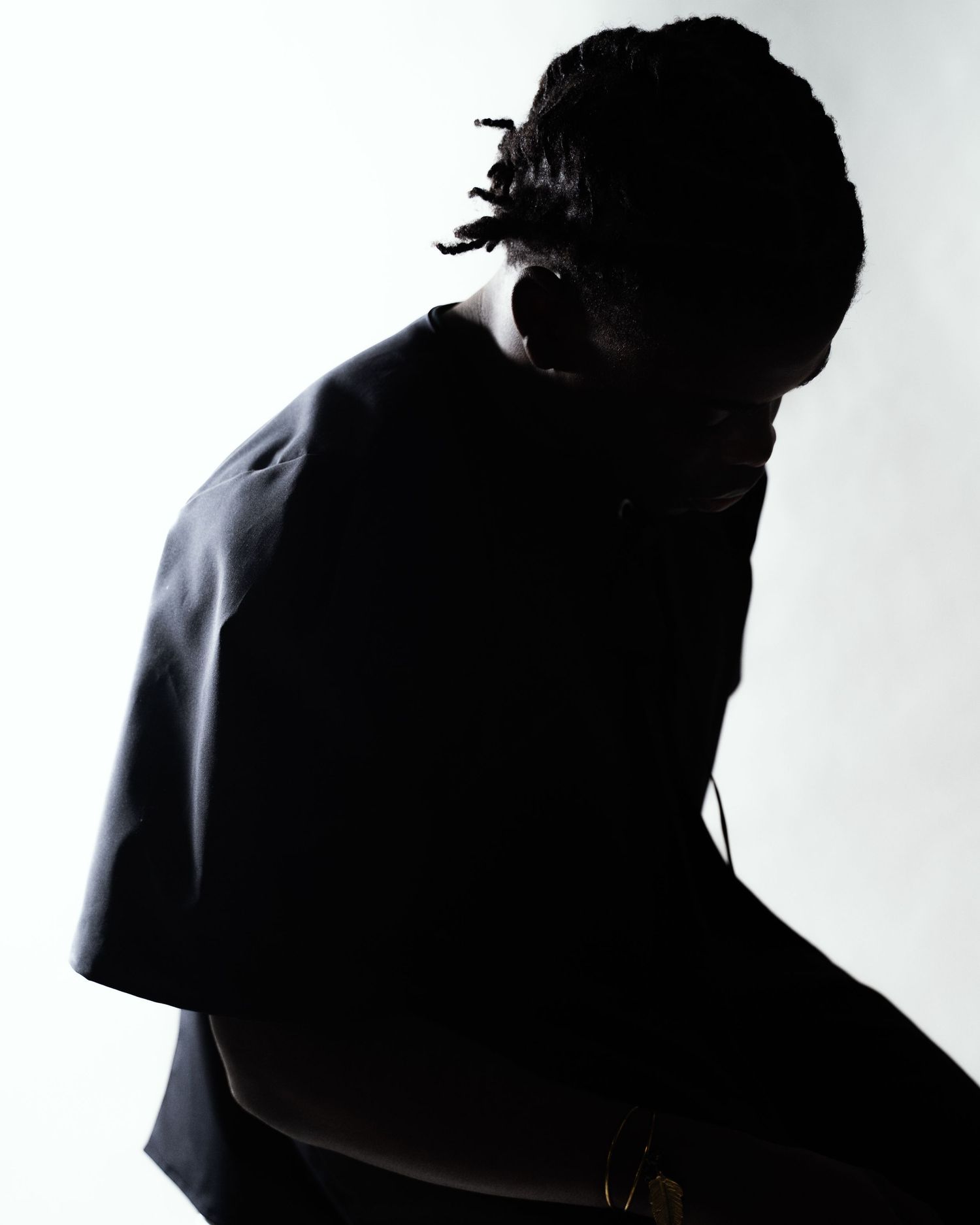 Dark silhouette of person with dreadlocks in black top.