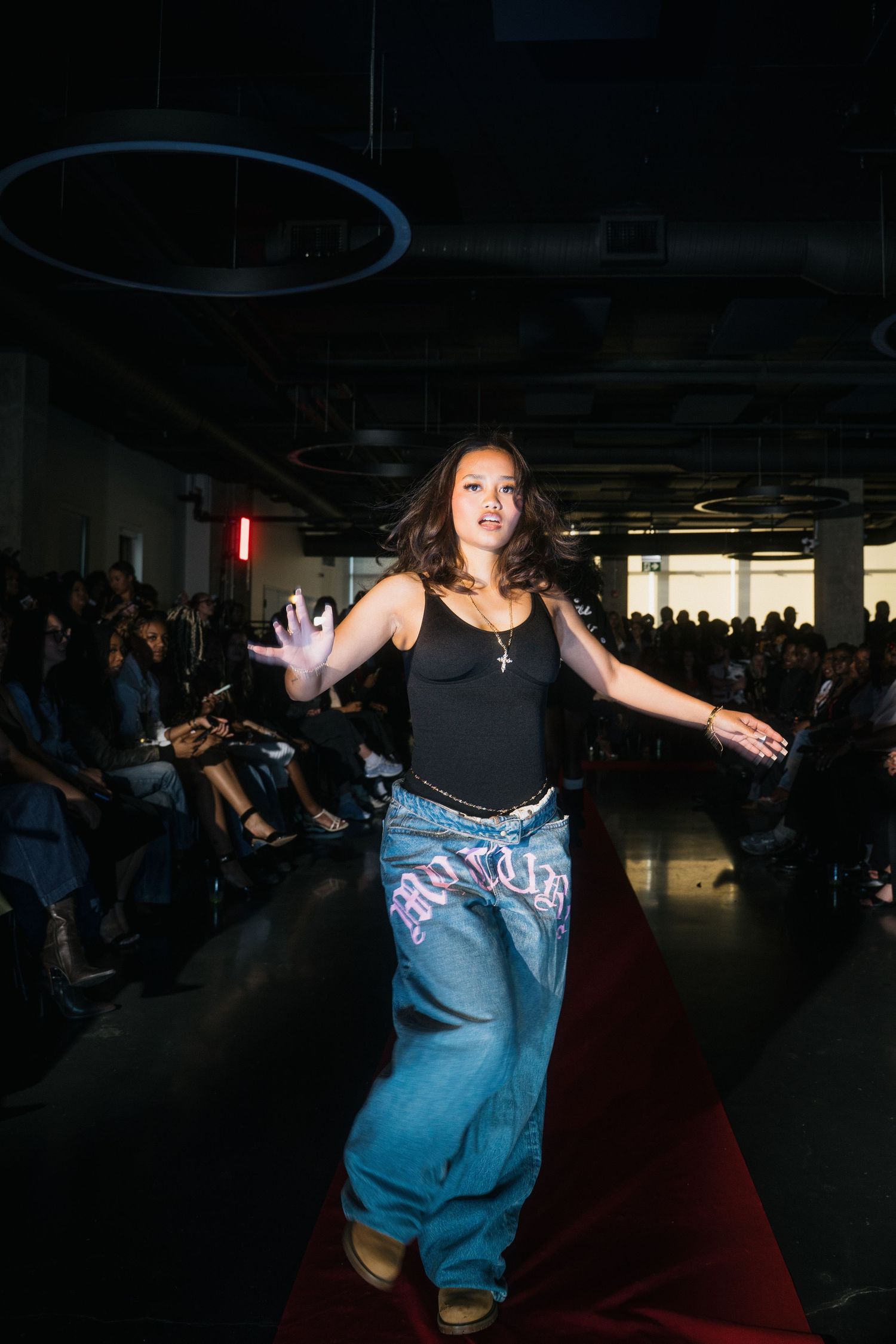 Female model struts runway in oversized blue graffiti jeans and black tank top at streetwear show.
