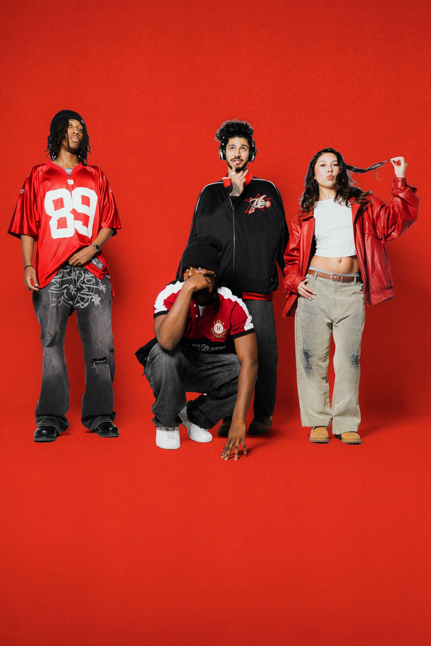 Three stylish young people posing in streetwear outfits against a bold red background in a fashion shoot.