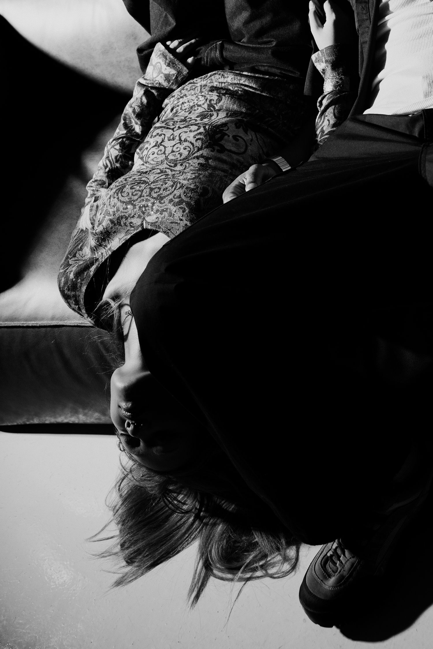 Black and white photo of a person hanging upside down off a sofa edge.
