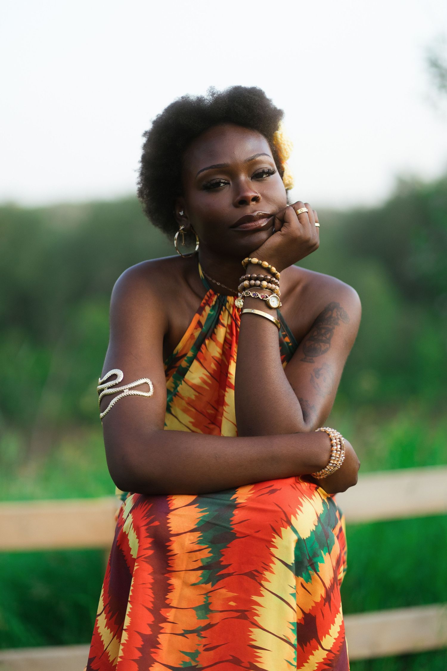A Black woman in a colorful African print halter dress poses outdoors with natural hair.