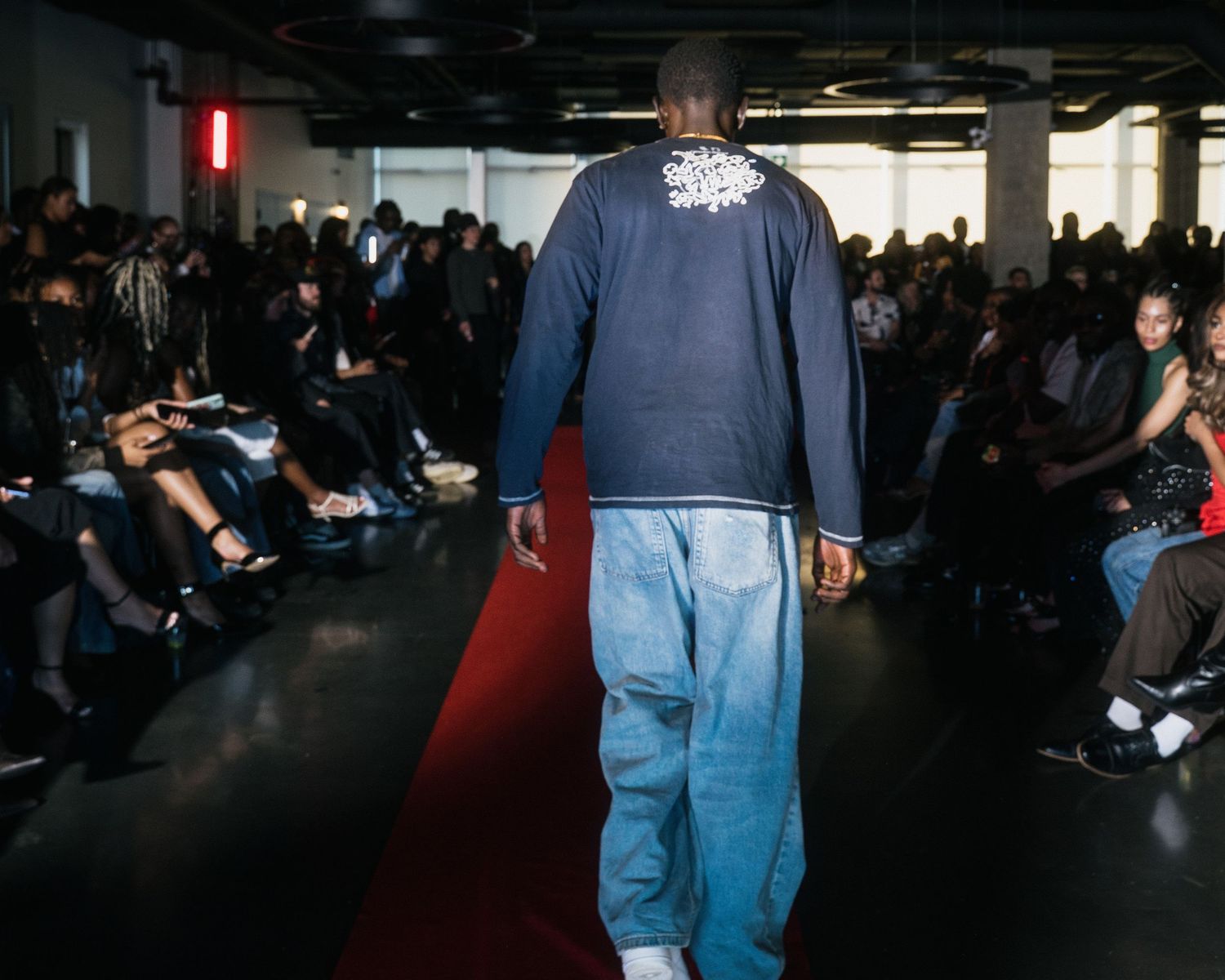 Rear view of male model in navy sweatshirt with floral collar detail on fashion runway.