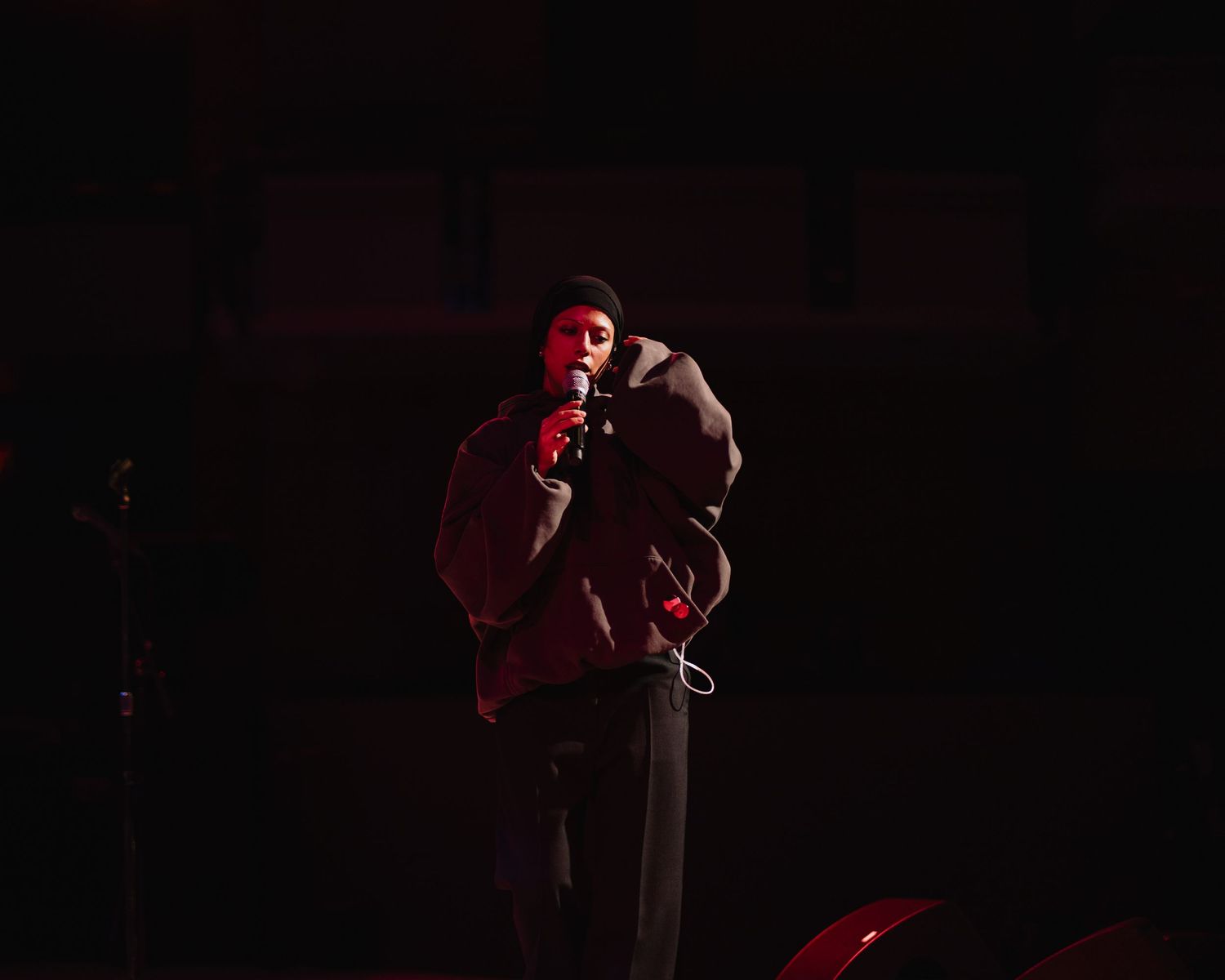A solo artist performs under dramatic red stage lighting while holding a microphone in both hands.