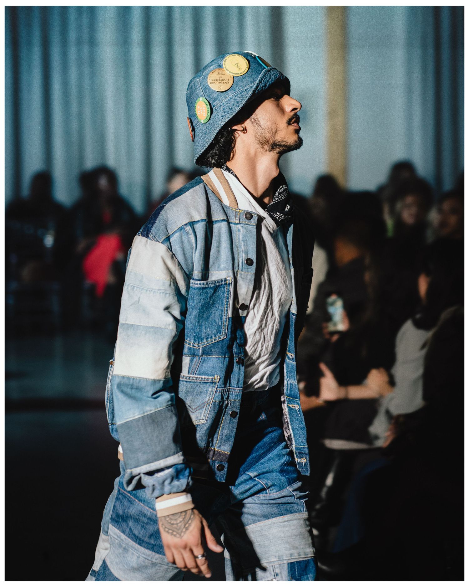 Close-up of male model in patchwork denim jacket and bucket hat on fashion runway.