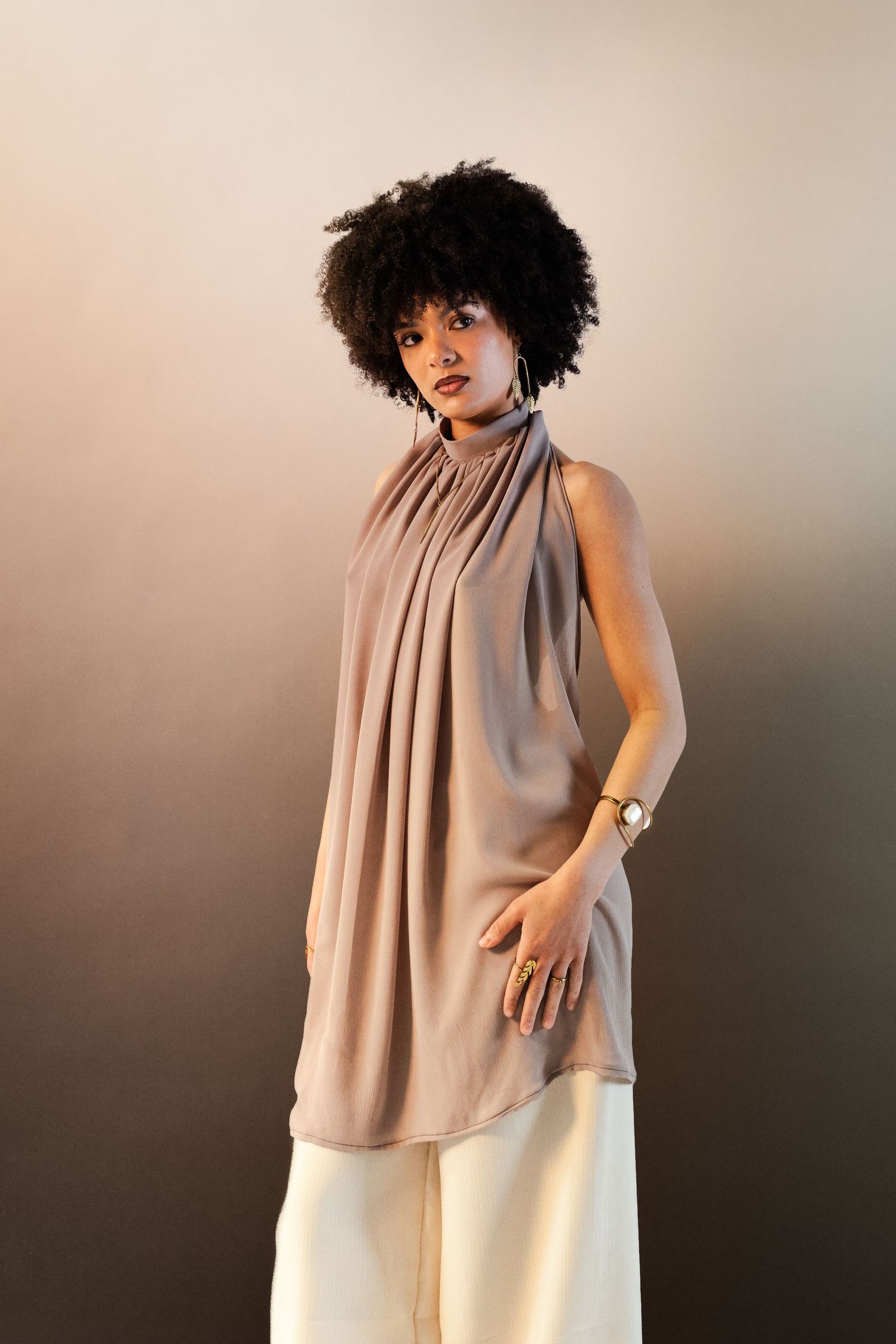 Woman with natural afro wearing sleeveless taupe draped top and white wide-leg pants.