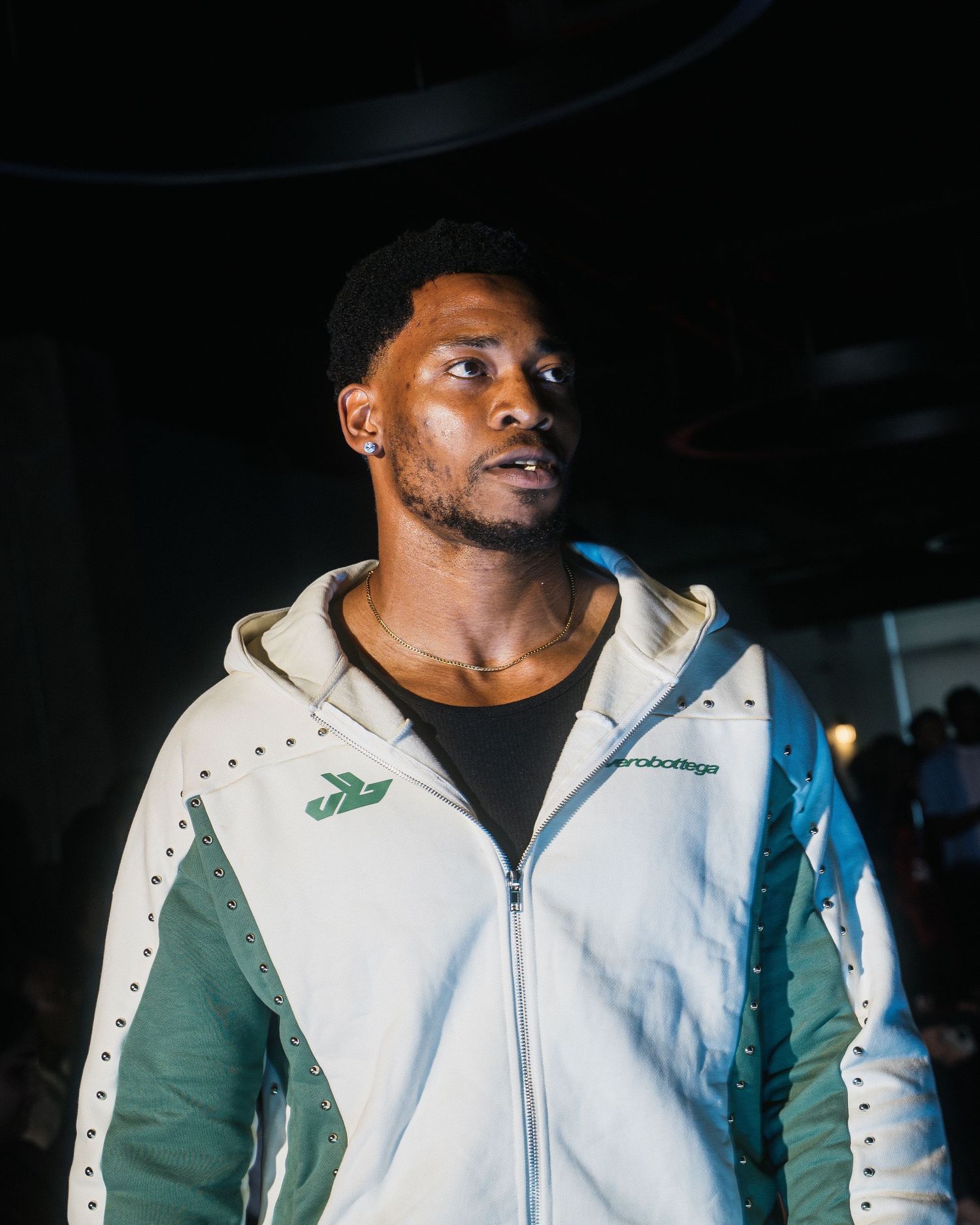 Male model in white and teal Bottega athletic jacket poses confidently at a fashion showcase.