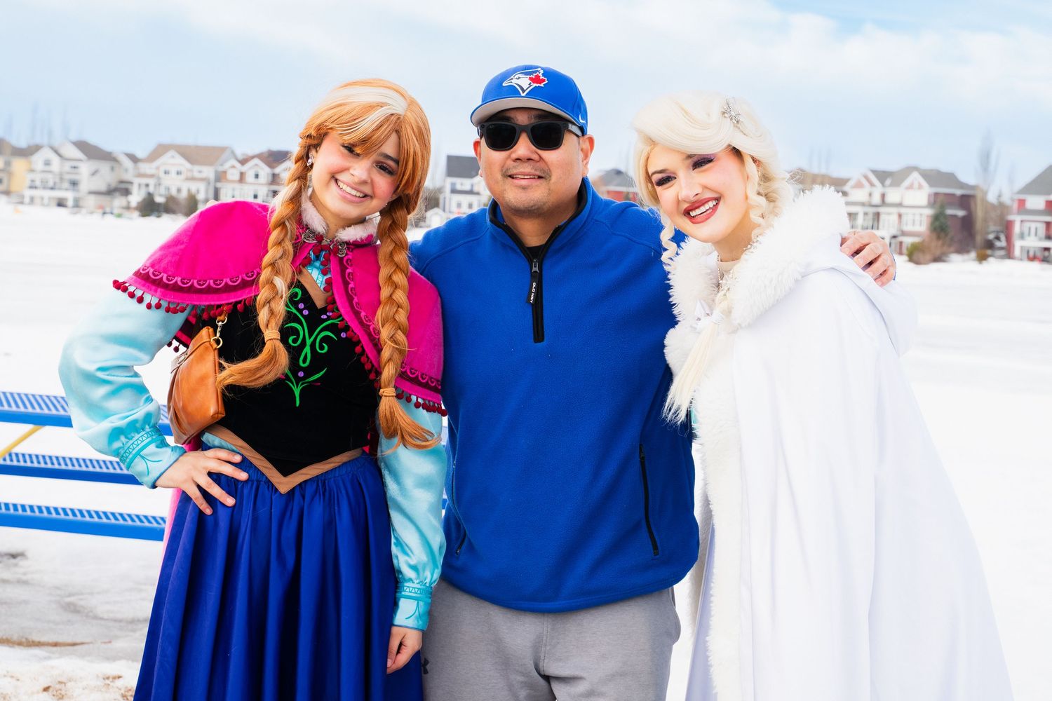 Man posing with Anna and Elsa Frozen character costumed performers in snowy outdoor winter setting.