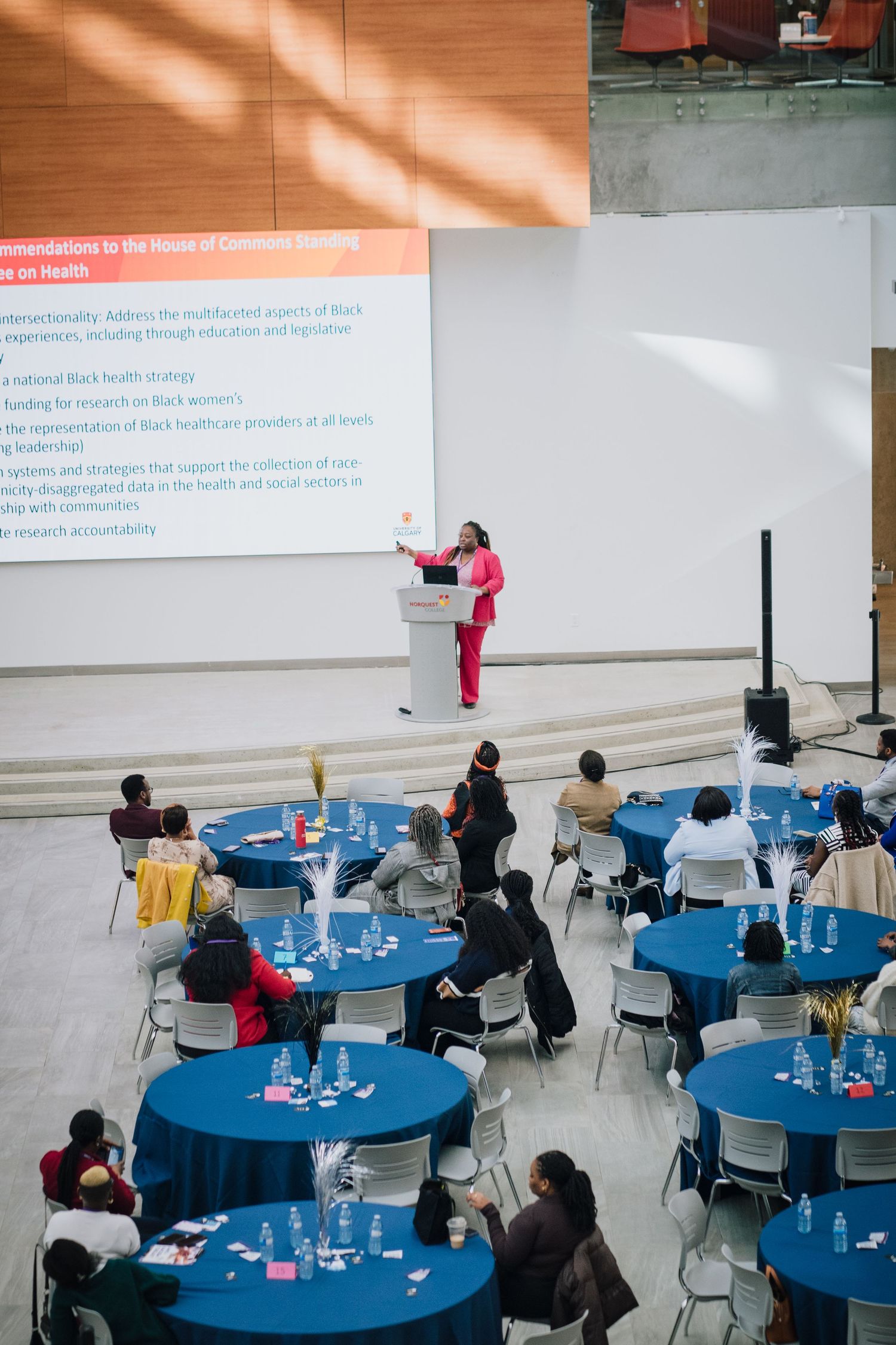 Speaker presents Black womens health recommendations at conference with blue round tables.