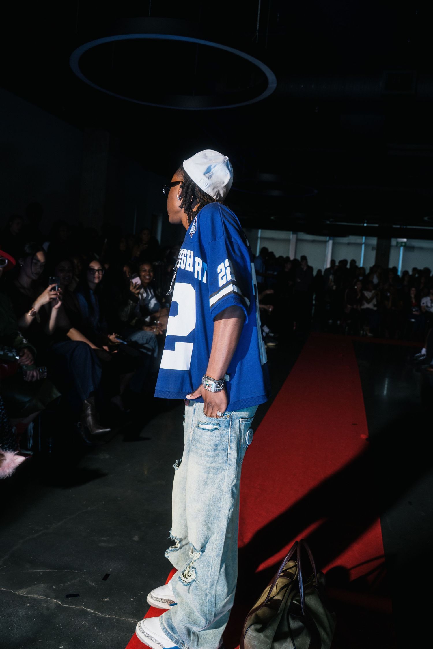 Male model seen from behind in blue number 22 jersey and distressed jeans on red runway.