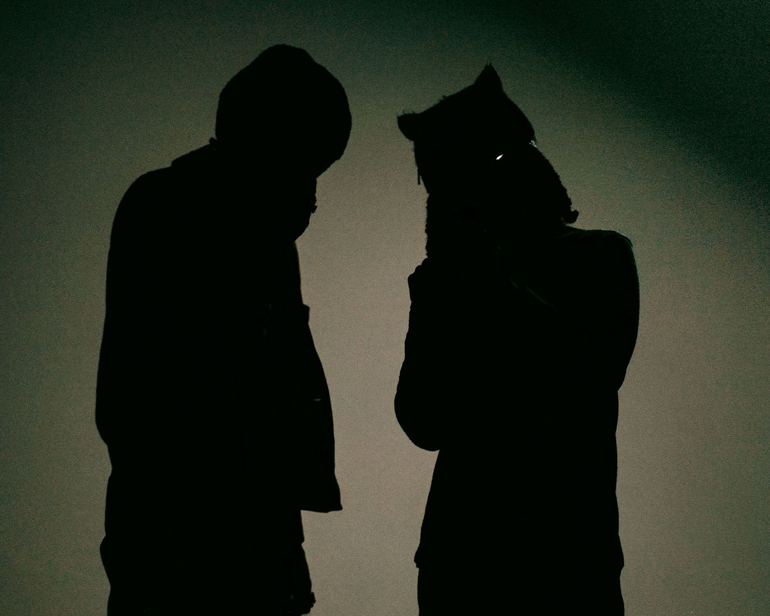 Two silhouetted figures standing close together in dramatic backlit shadow photography.