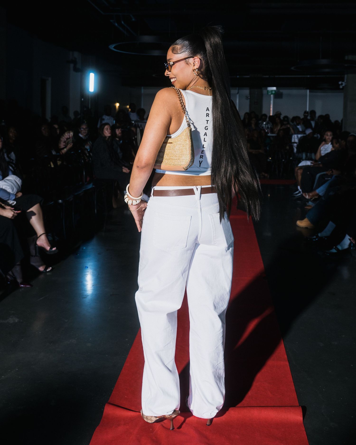 Female model in white wide-leg pants and crop top walking away on a red carpet fashion runway.