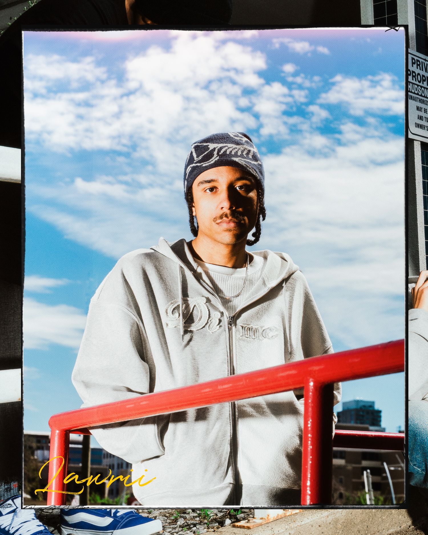 Photo print of young man in grey hoodie and beanie held up against matching outdoor backdrop.