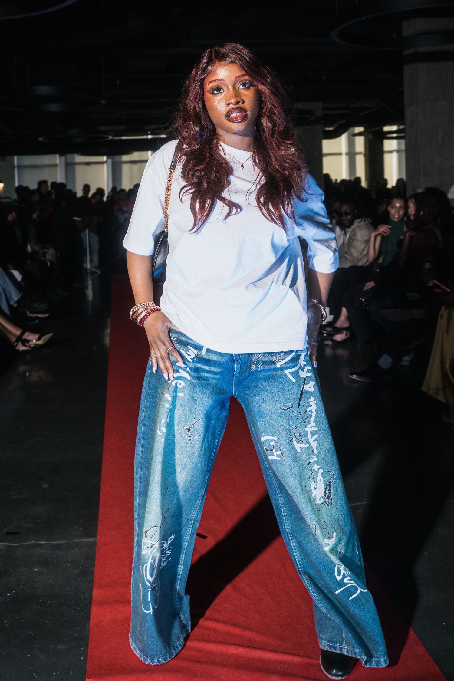 Model poses on red carpet runway wearing white oversized tee and wide-leg graffiti denim jeans.