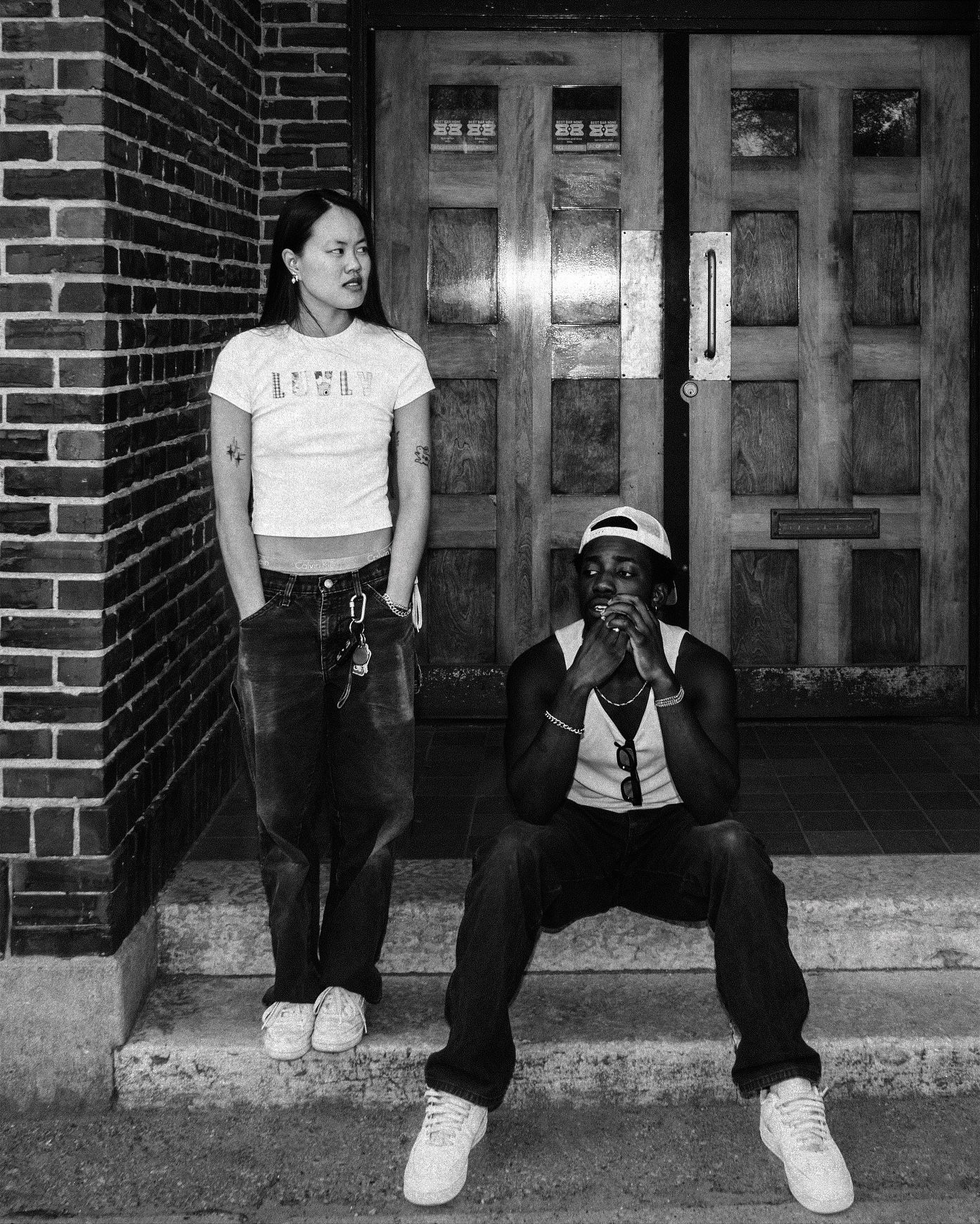 Black and white photo of two young people posing on steps outside a brick building.