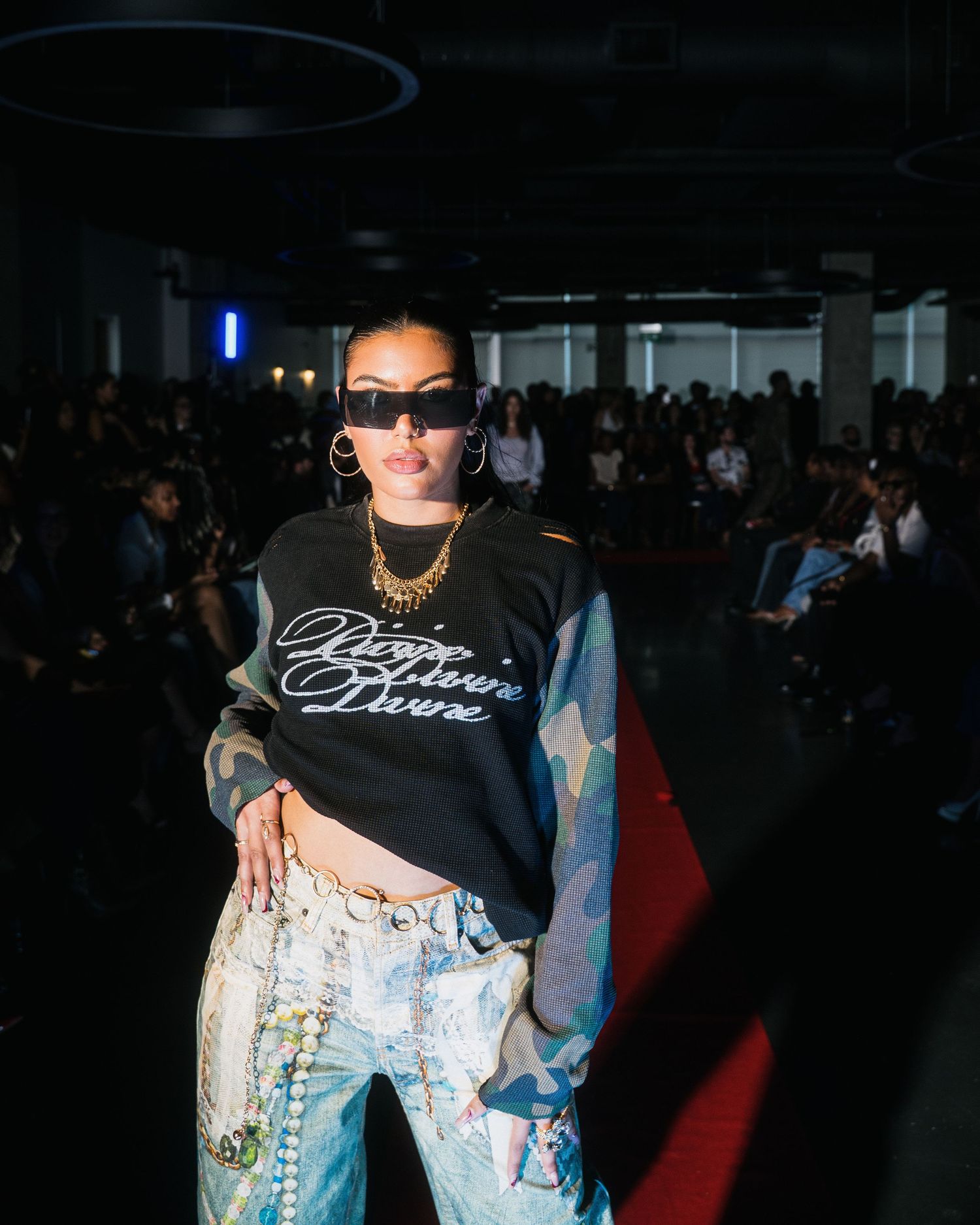 Model wears black script graphic sweatshirt with artistic printed jeans at streetwear fashion show.
