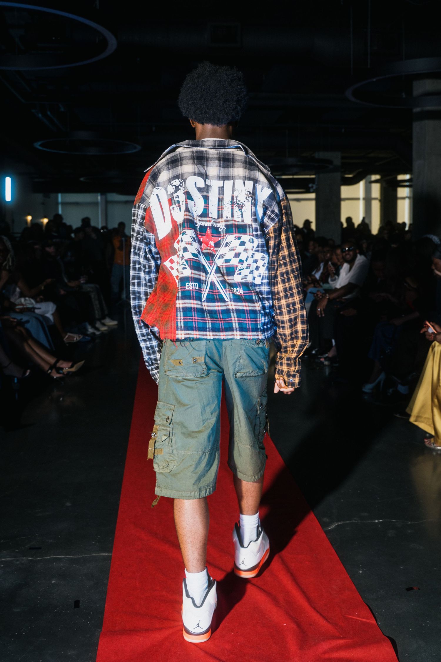 Model walks red carpet runway in patchwork plaid jacket and cargo shorts with Jordan sneakers.