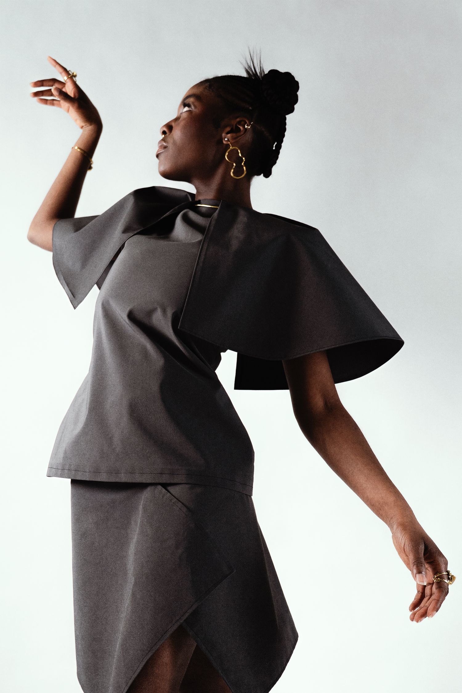 Woman in structured gray cape top and asymmetric skirt posing.