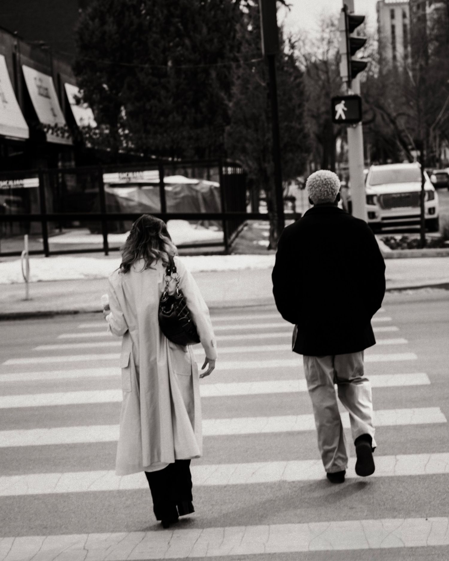 Two people in winter coats crossing a city street crosswalk in black and white photography.