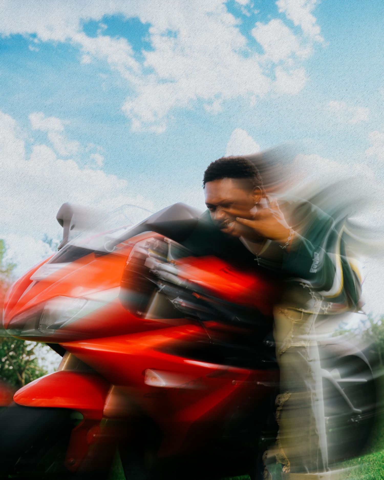 Motion blur photo of a person leaning on a red motorcycle under a cloudy sky.