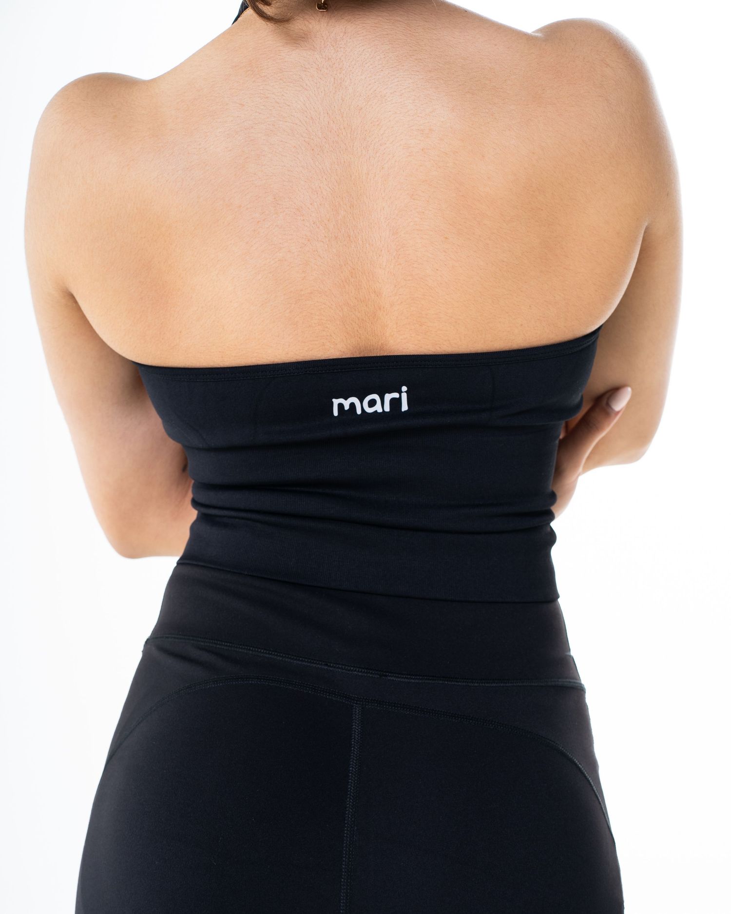 Back view of a woman wearing a black strapless Mari branded bandeau top and leggings.