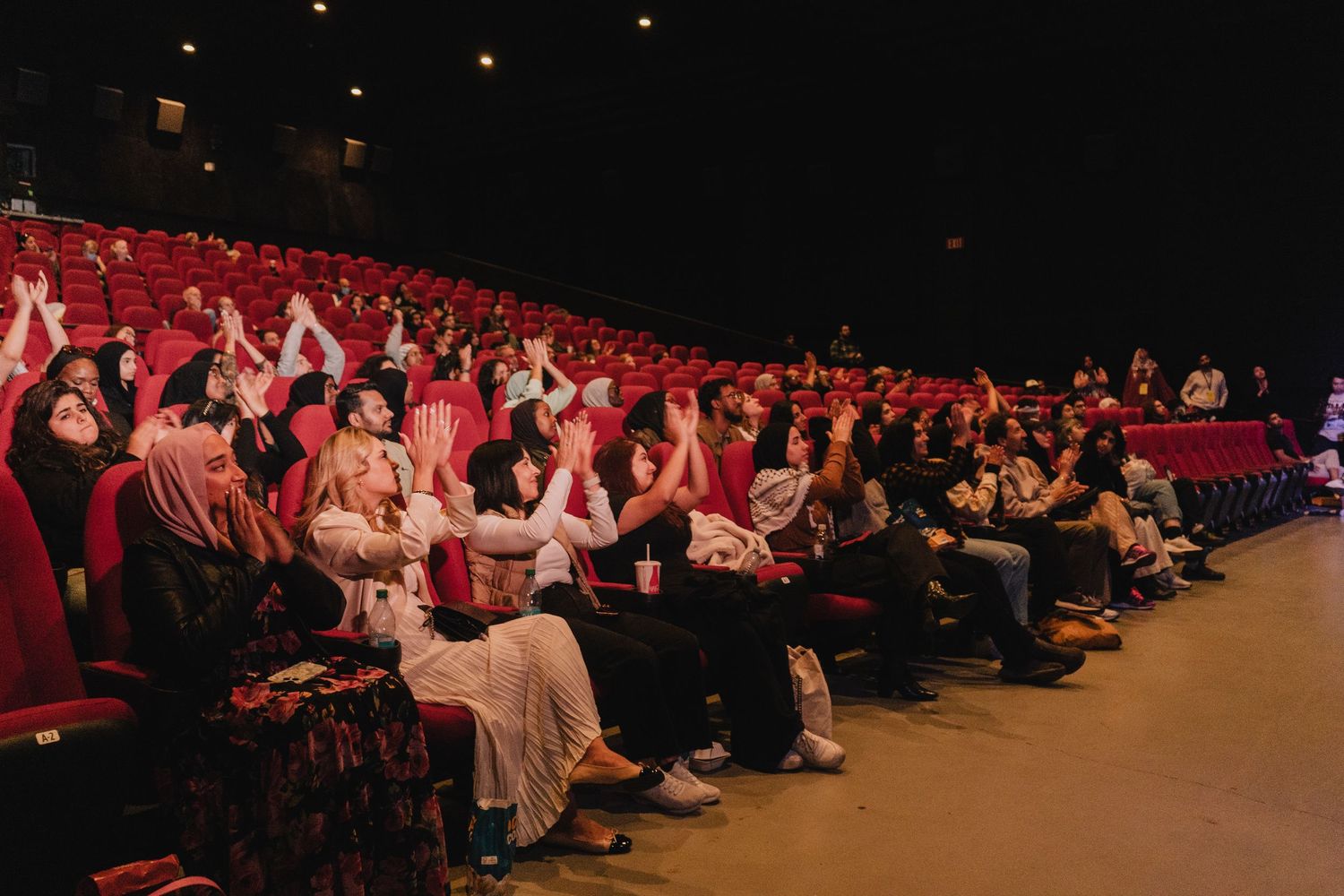 A diverse audience applauds and cheers in a red-seated theater during a film festival screening.