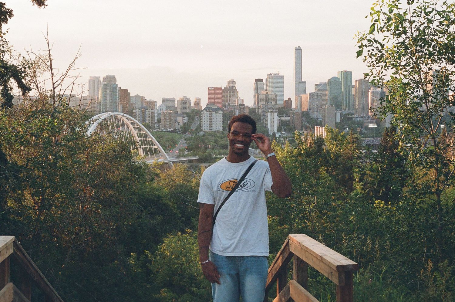 Smiling man in white t-shirt poses on wooden deck with city skyline backdrop.