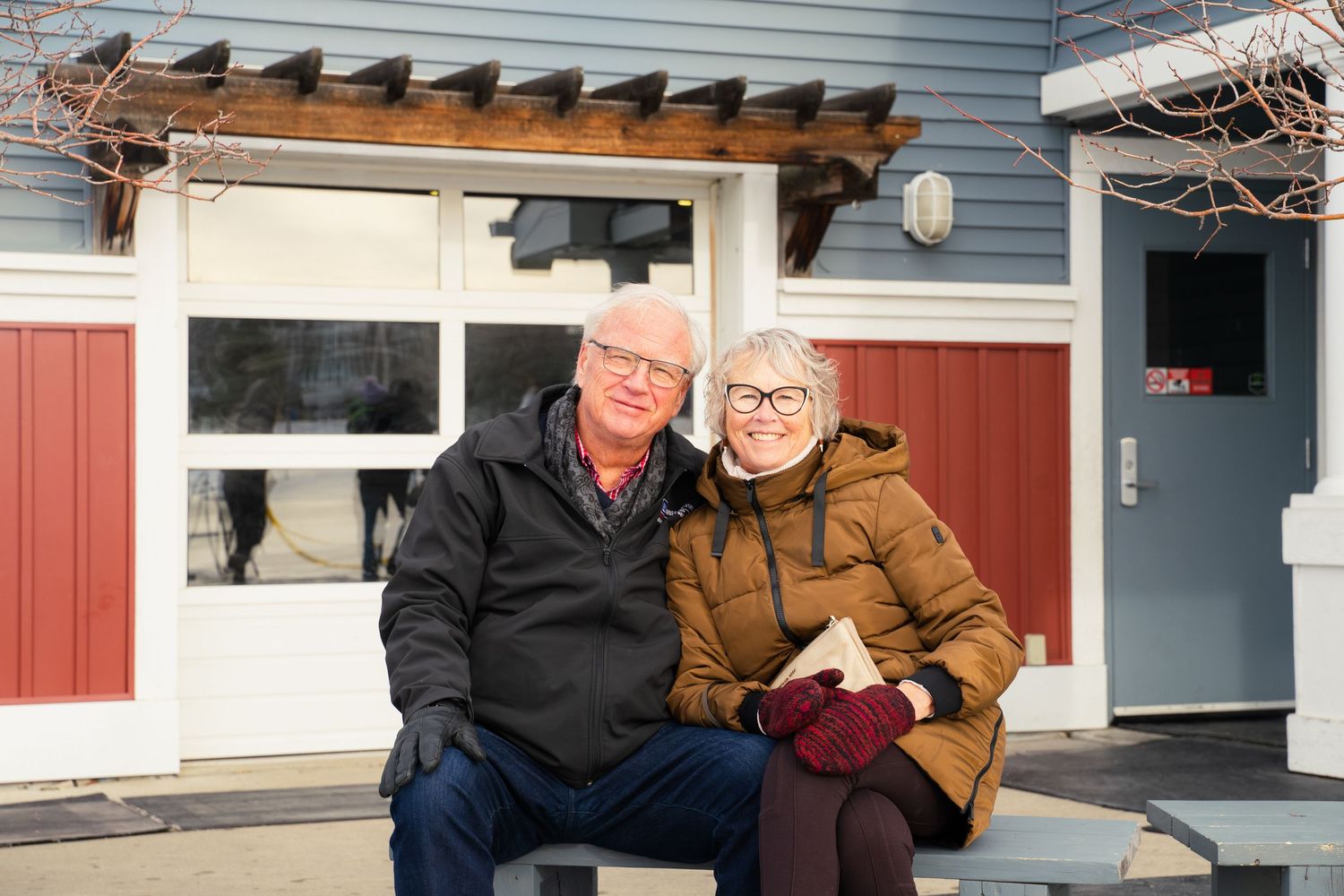 Older couple smiling and sitting together outside a blue and red building.