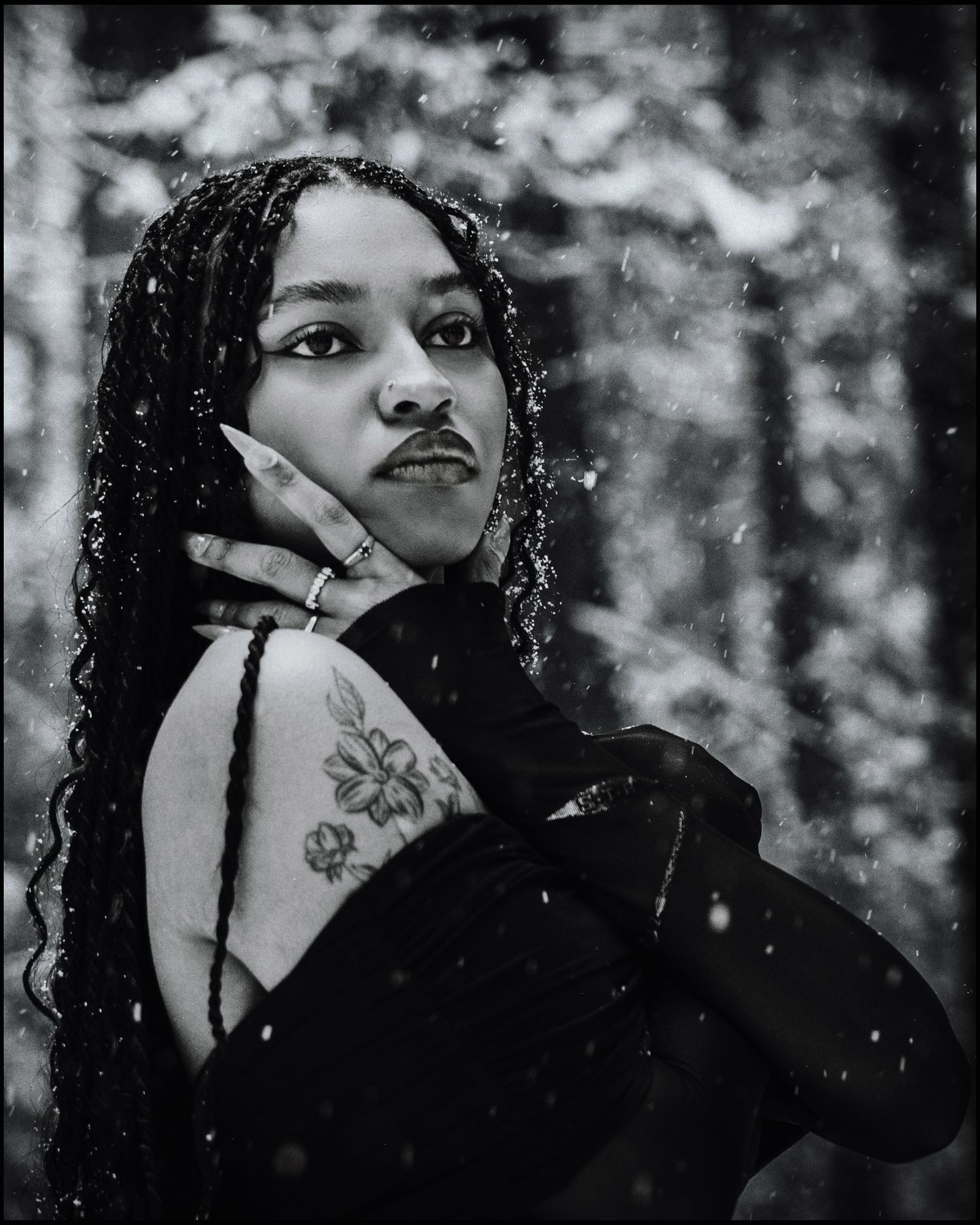 Black and white portrait of woman with braids and floral shoulder tattoo in snow.