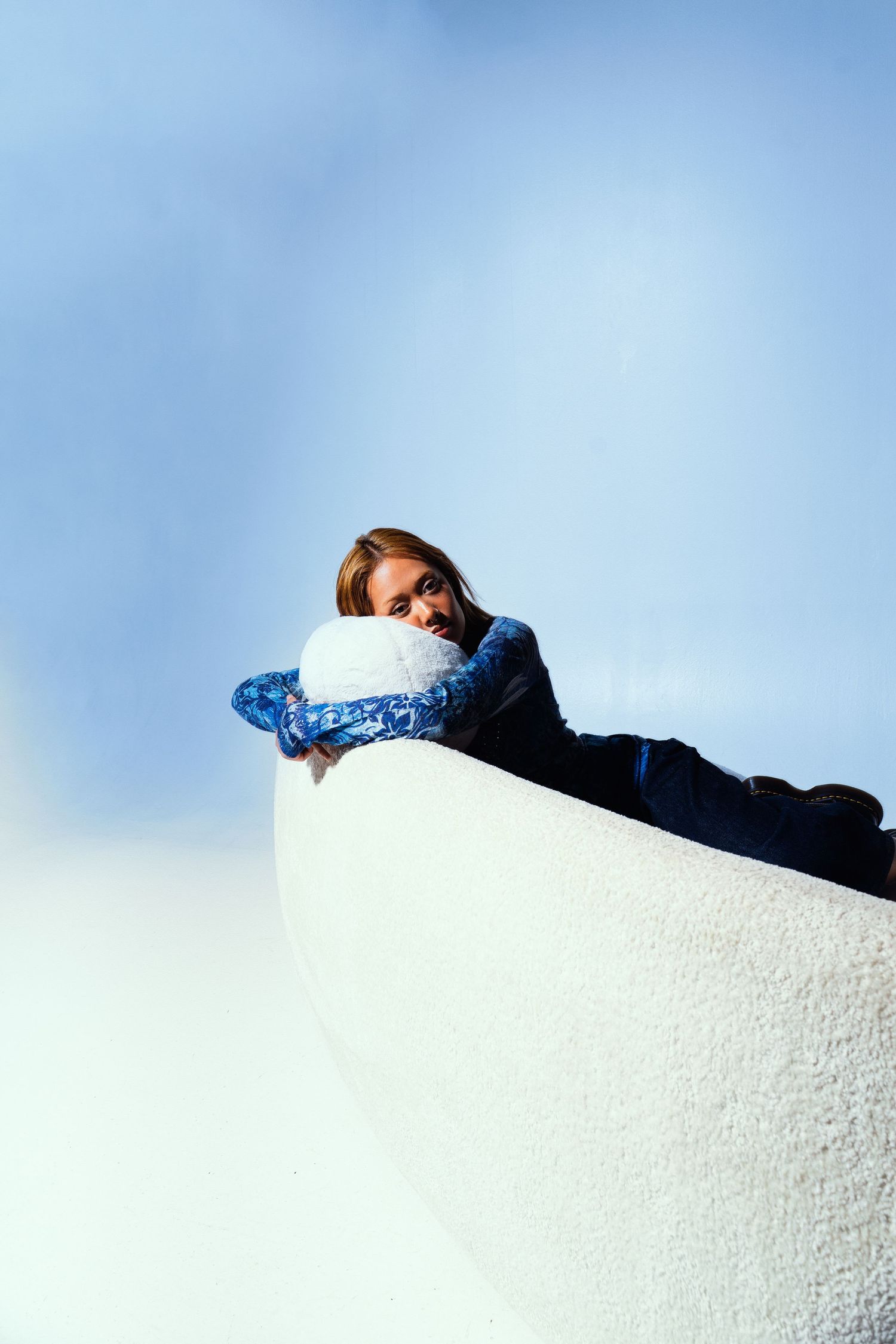 Person in blue floral jacket resting on white curved wall against bright sky.
