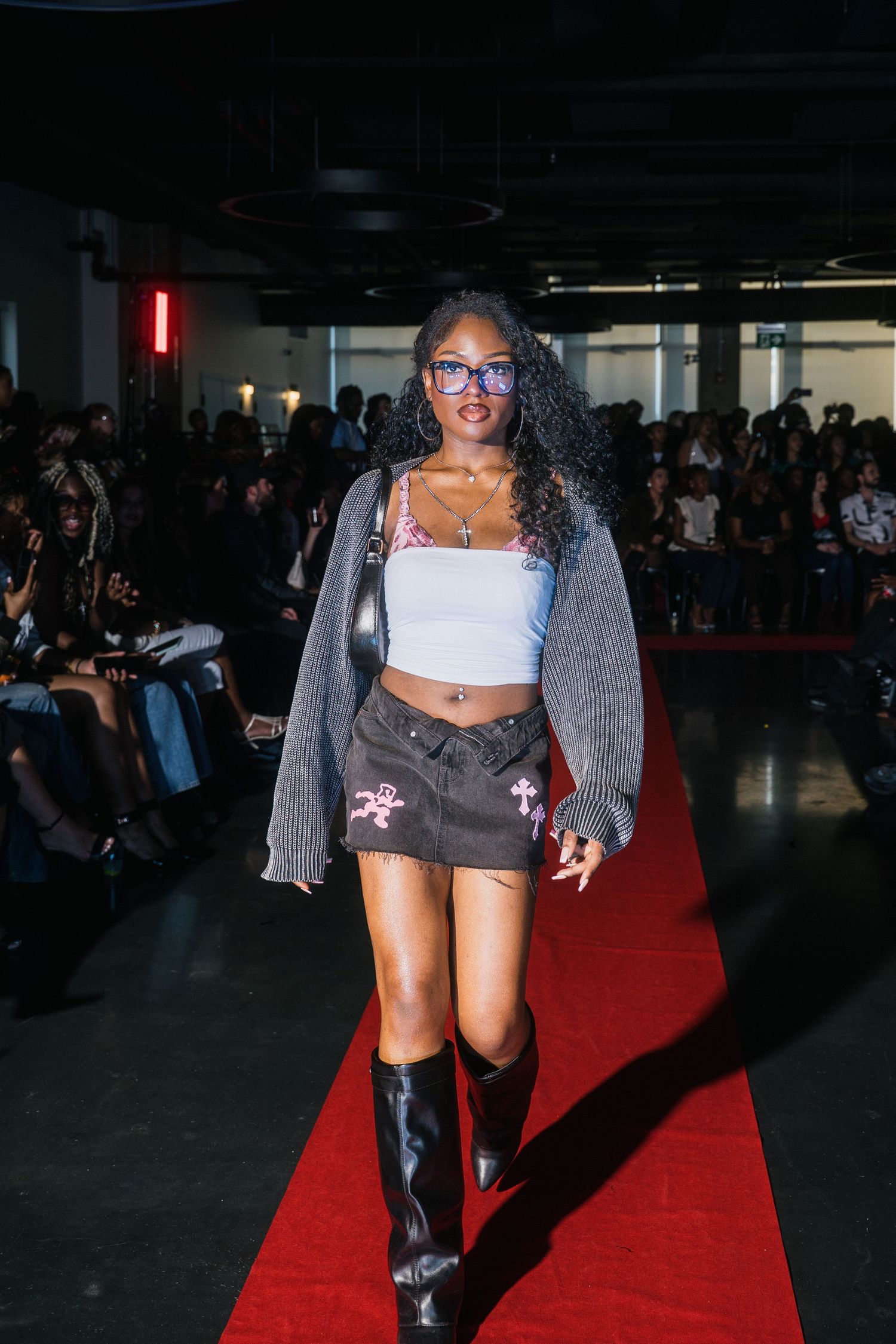 Model struts runway wearing gray cardigan, white crop top, dark mini skirt and knee-high boots.