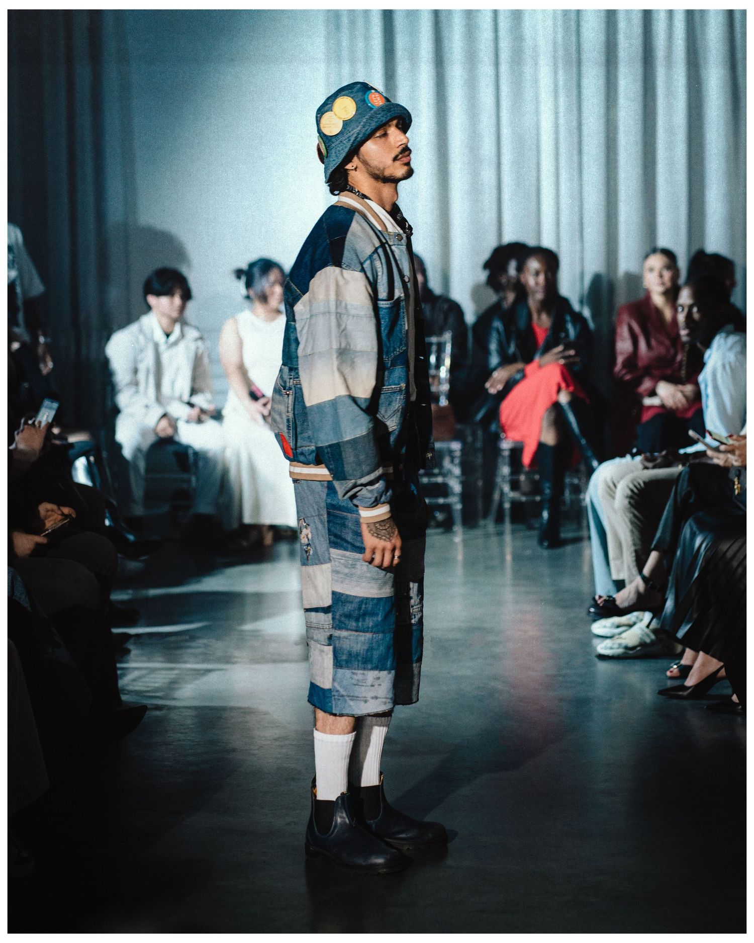 Model poses on runway in patchwork denim ensemble with bucket hat and black boots.