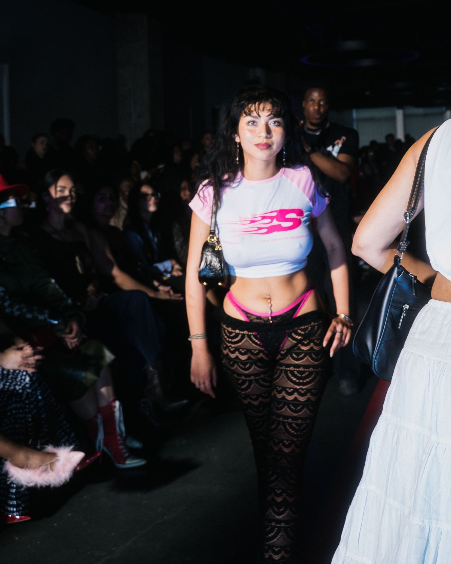 Female model walks fashion show runway in tie-dye crop top, pink underwear, and black lace pants.