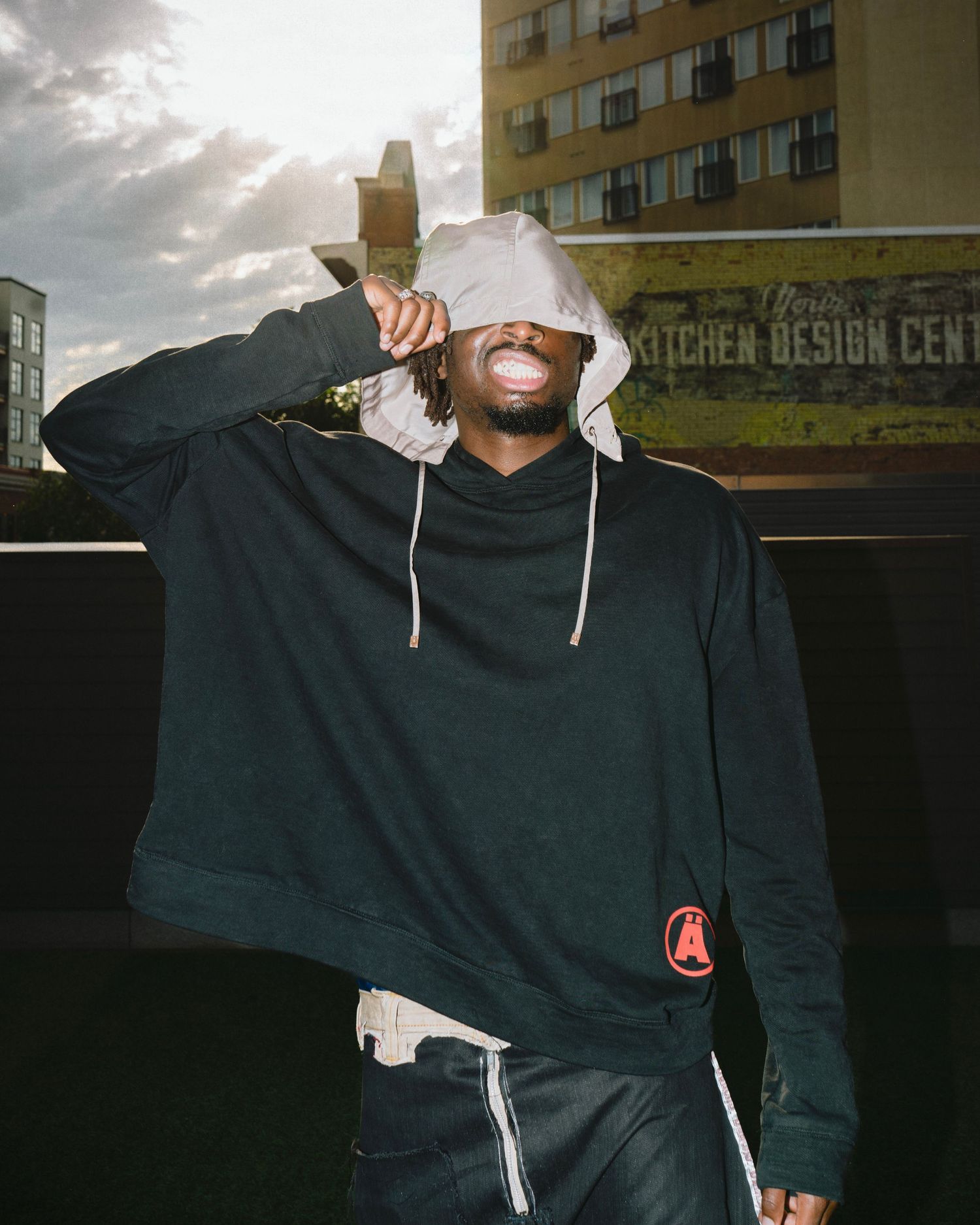 Man in black hoodie blowing bubble gum on rooftop with urban background.