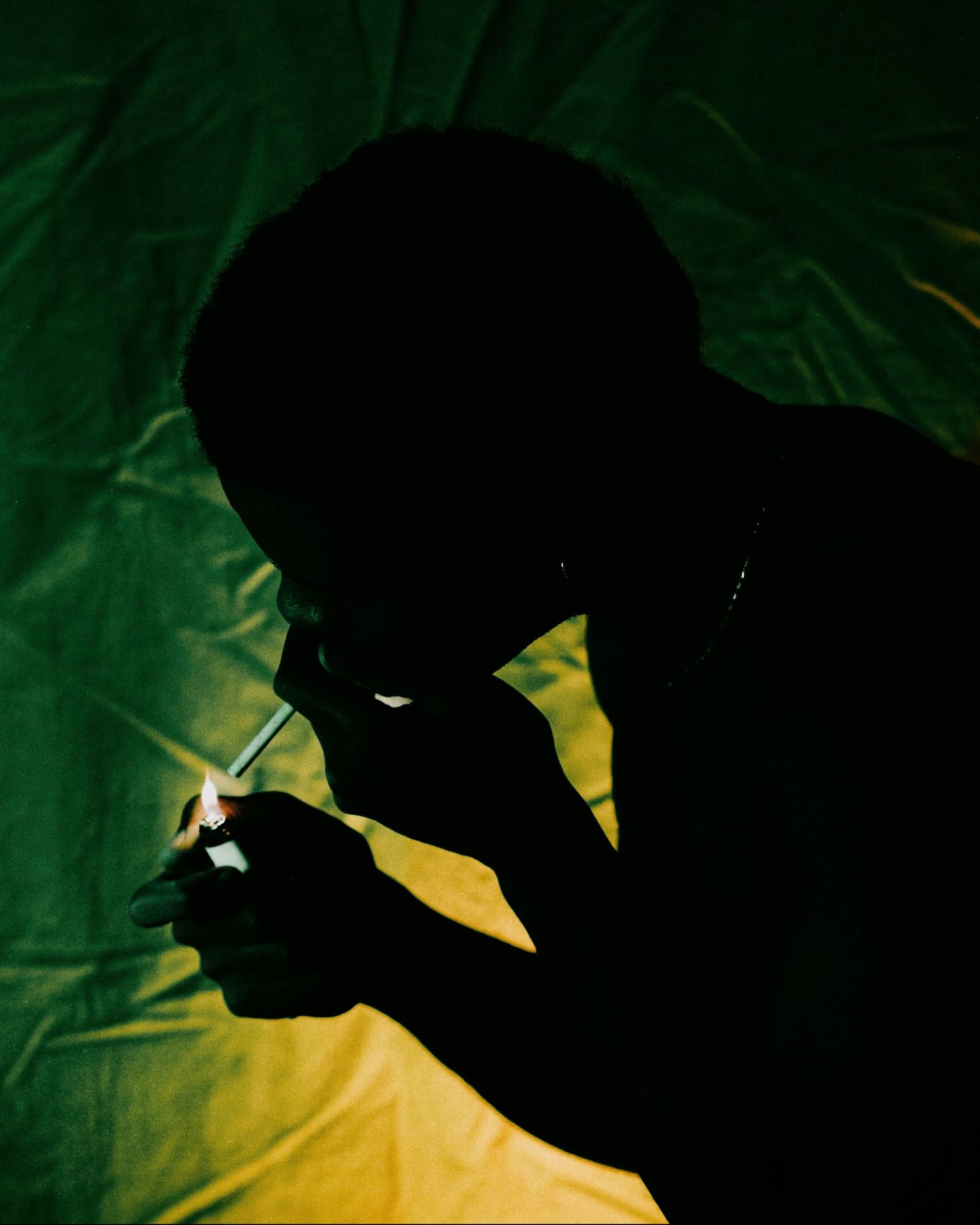 Silhouette of person lighting something against green and yellow fabric background.