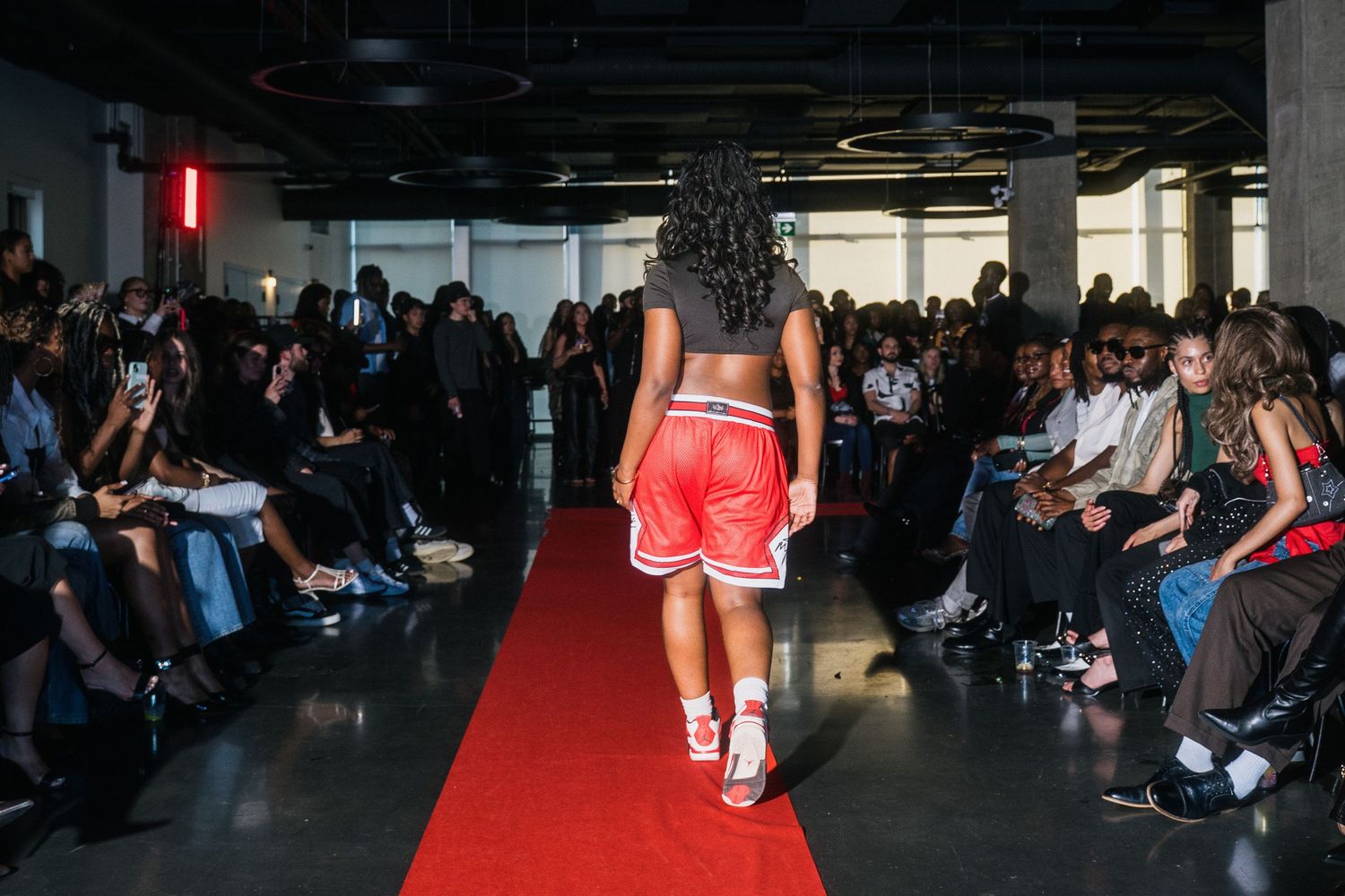 Rear view of model in red athletic shorts and crop top walking fashion show runway.