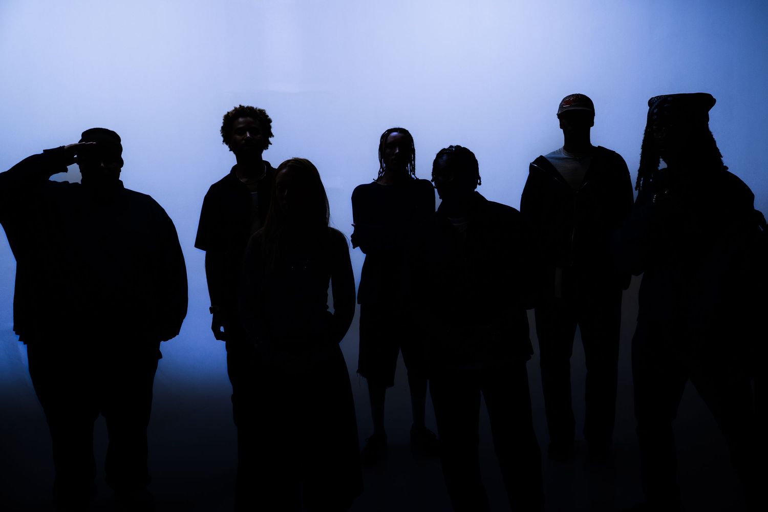 Silhouettes of a group of people standing together against a dramatic blue-lit background.
