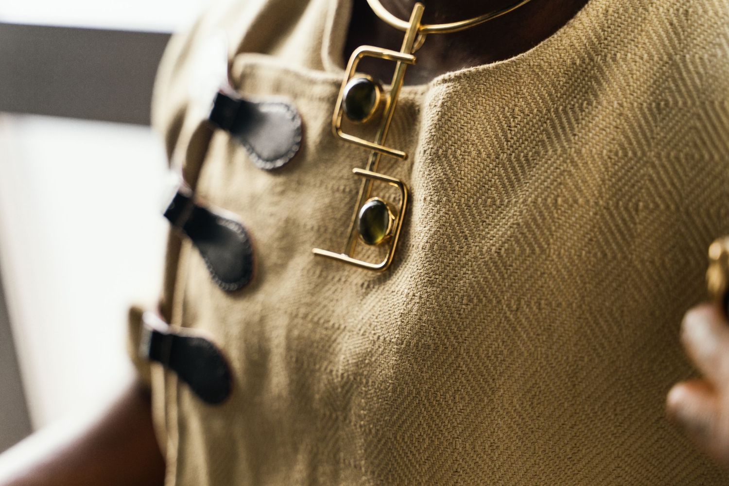 Close-up detail of gold diamond-pattern fabric vest with black toggle closures and gold safety pin hardware.
