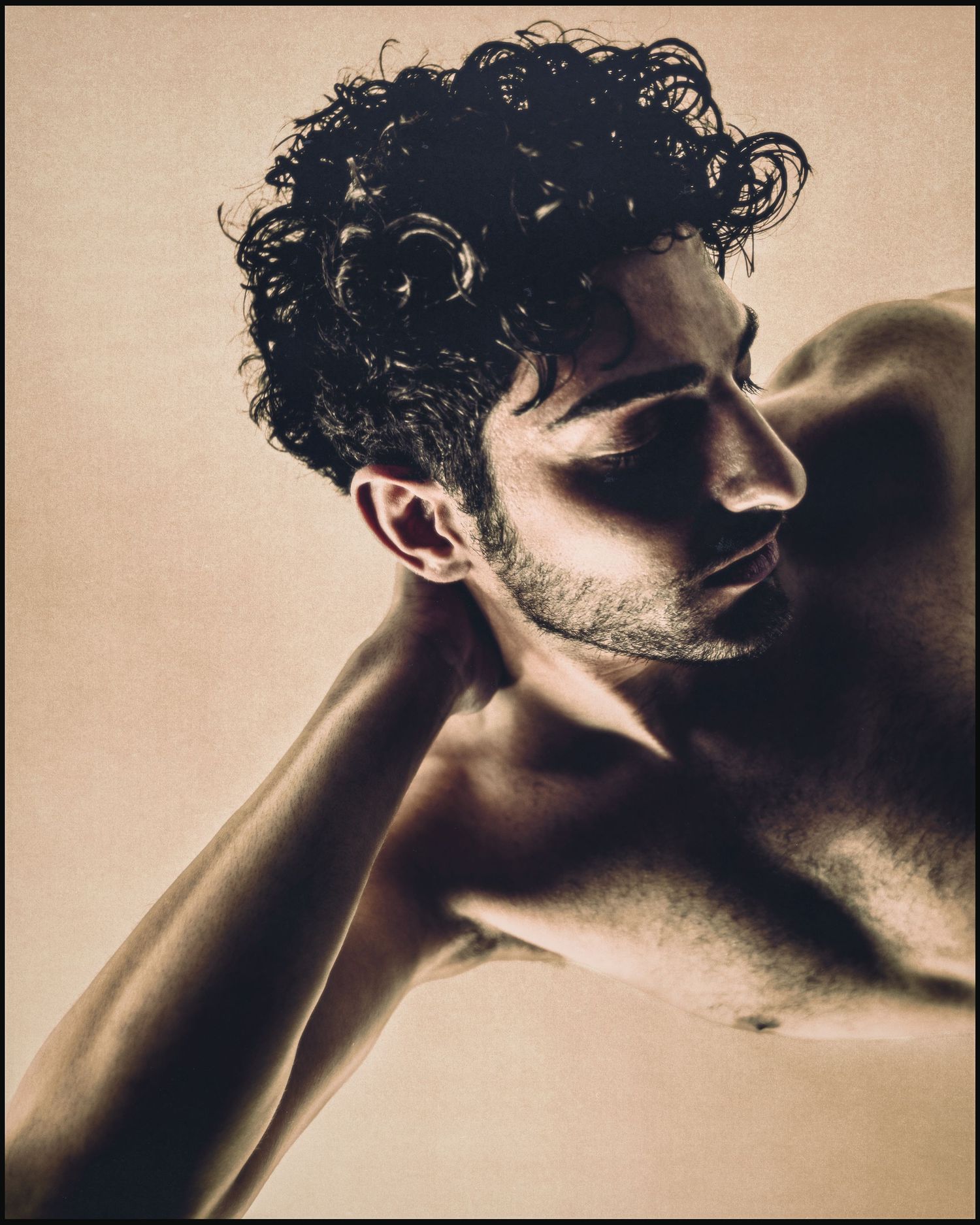 Artistic sepia portrait of curly-haired man with eyes closed in dramatic lighting.