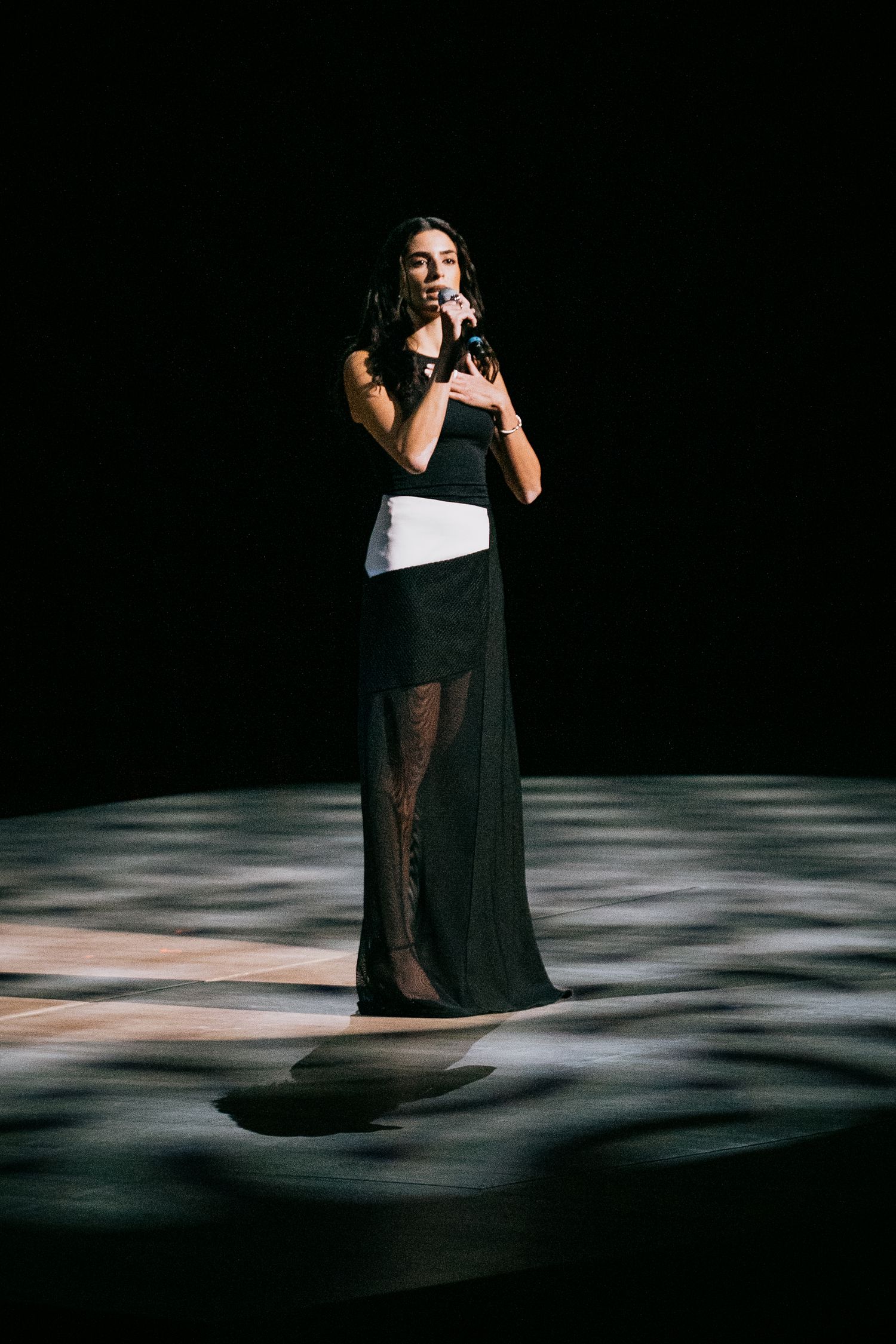 Singer in black and white gown performs on spotlight-lit stage during an elegant live music event.