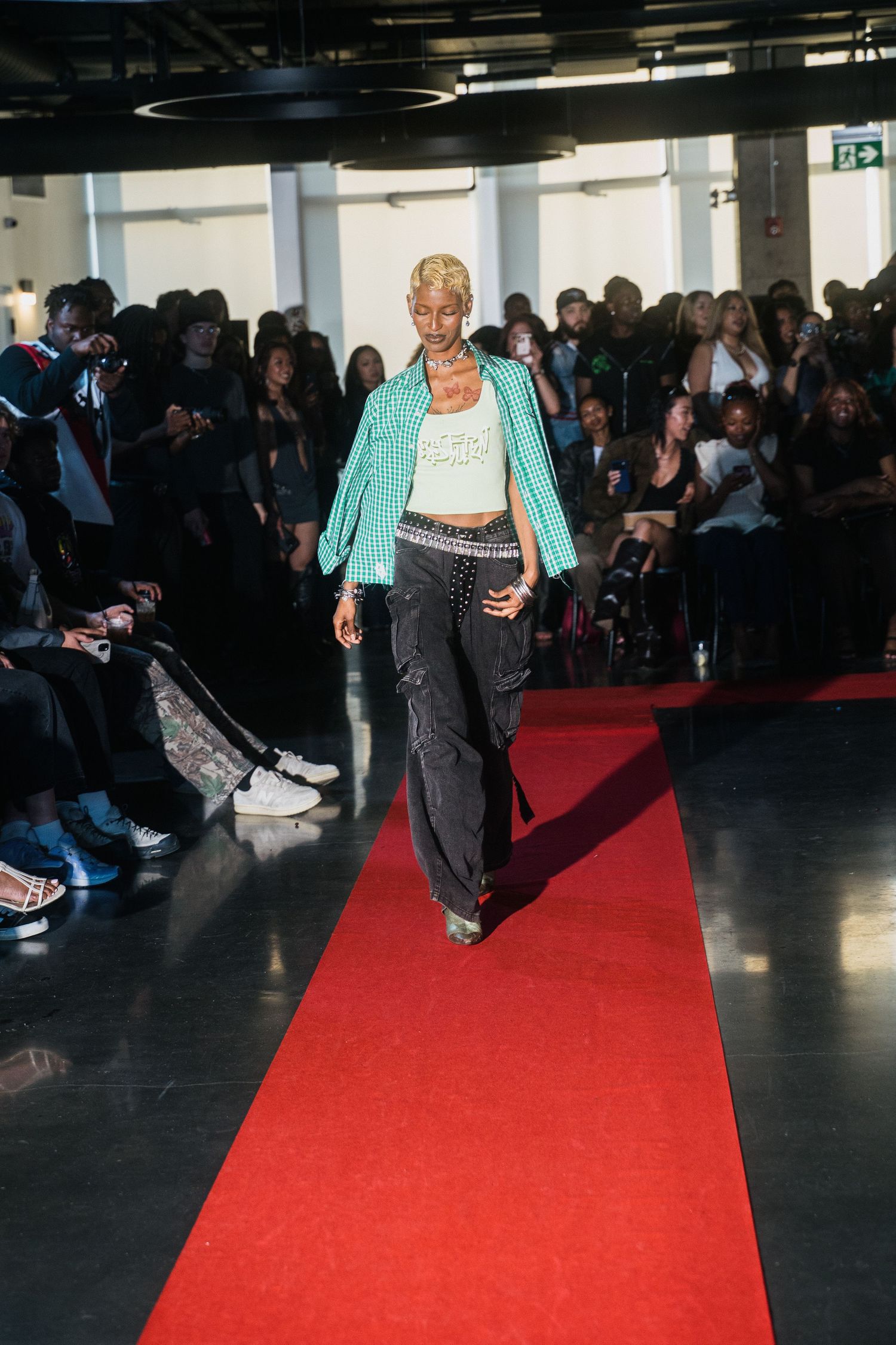Model walks red carpet runway in turquoise blazer, white crop top, and dark flared jeans.