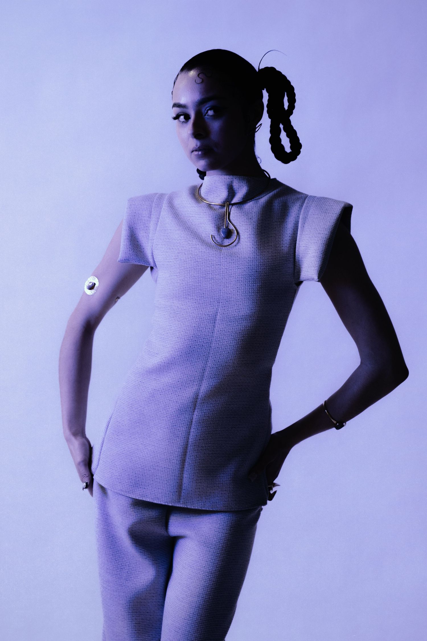 A woman in a lavender structured pantsuit poses confidently against a purple background.