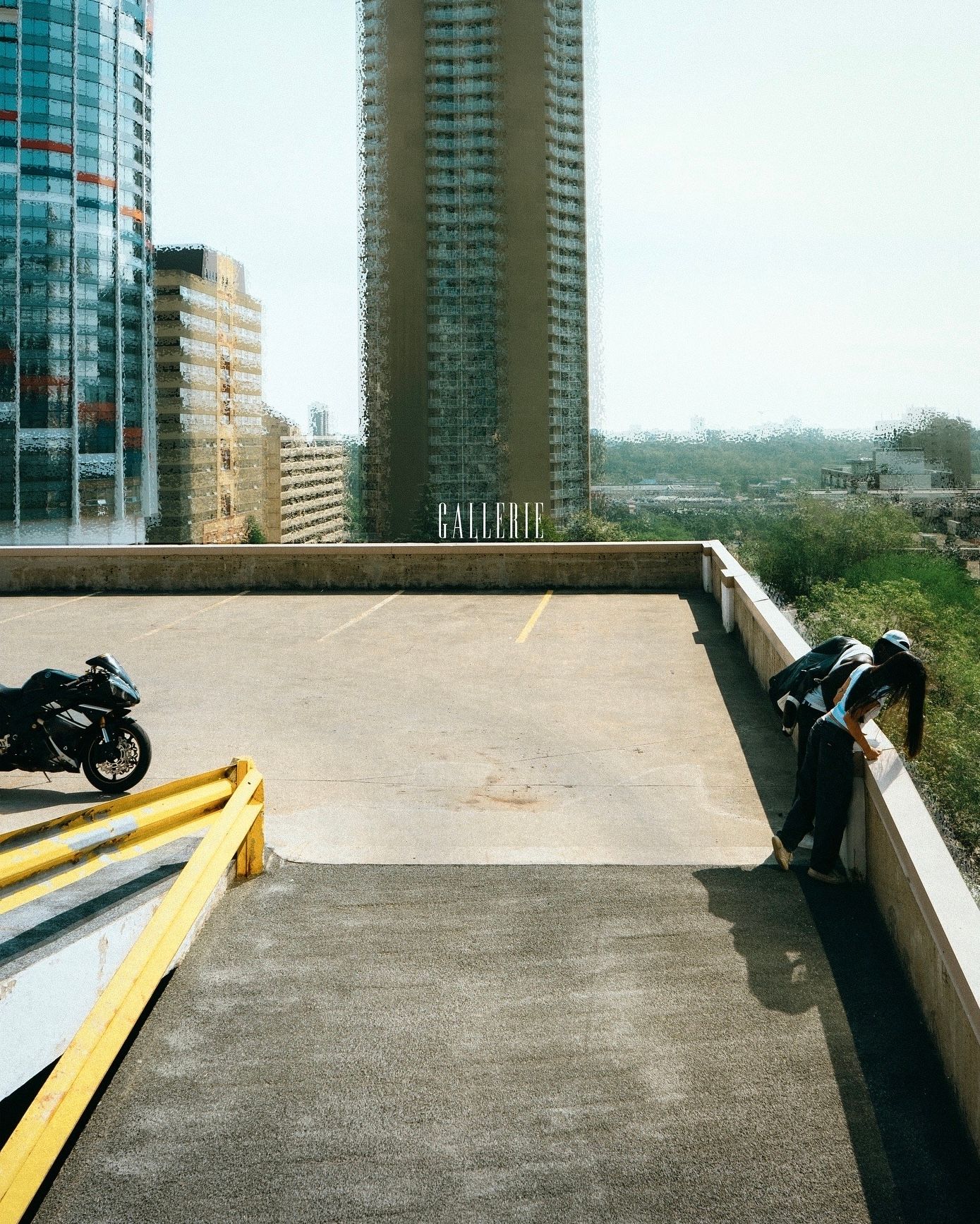 Person crouching on a rooftop parking lot with a motorcycle and city skyline in the background.